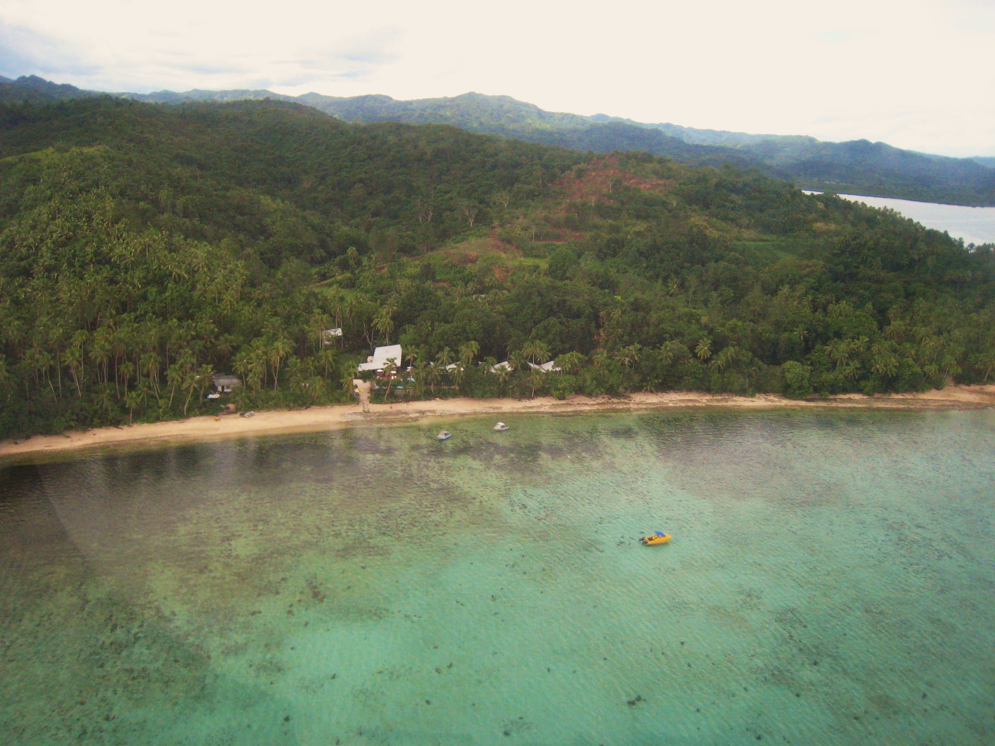 A calm reef-fringed beach with palms and a low resort, hills behind