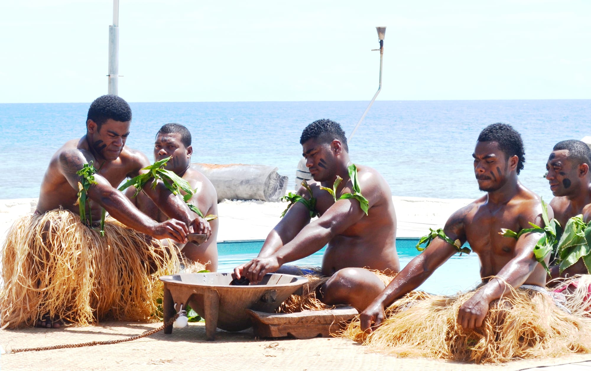 A group seated on the ground around a large wooden bowl during a ceremony