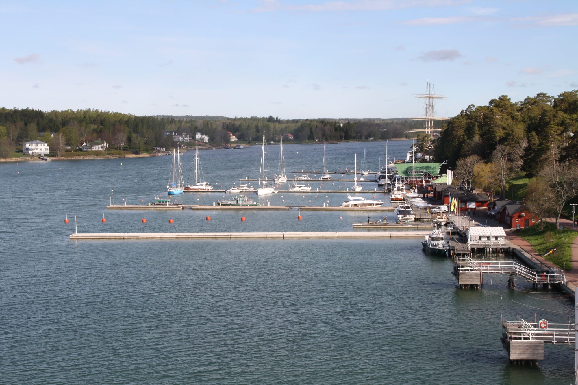 Tall-ship masts and small boats in a calm harbour under a clear sky