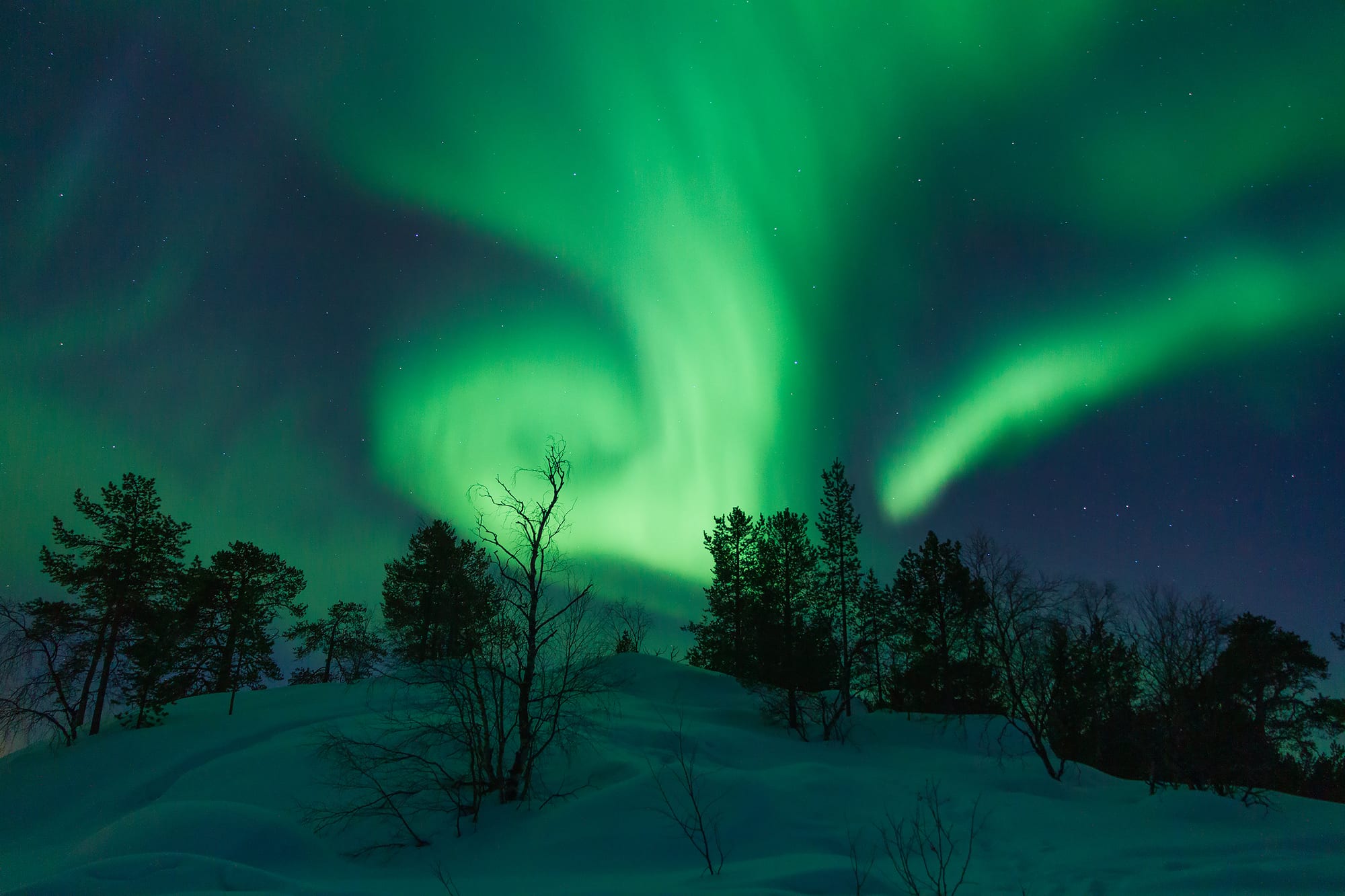 Green curtains of aurora swirling over a dark frozen lake and low hills