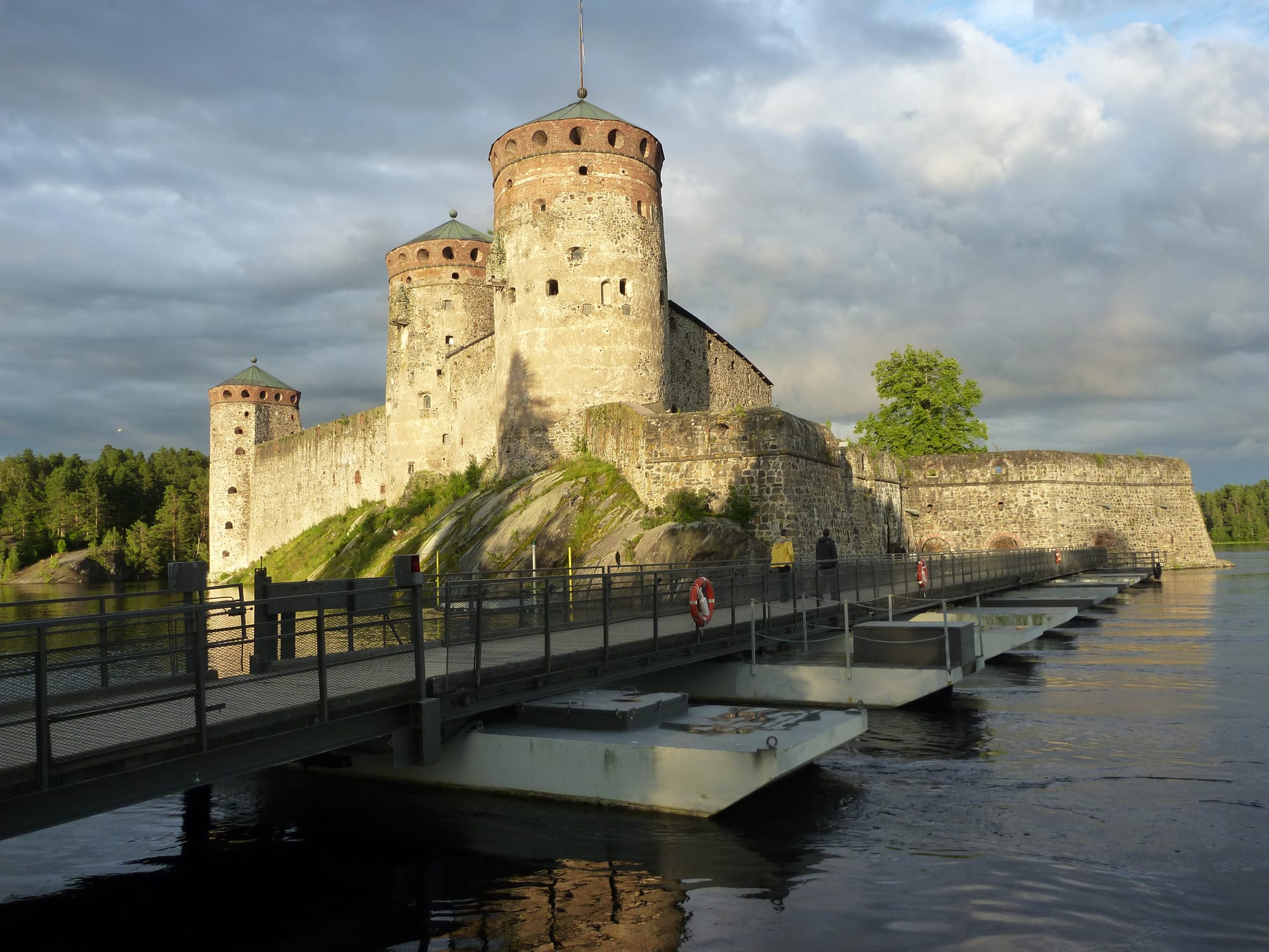 A grey stone medieval castle with round towers rising straight out of a lake