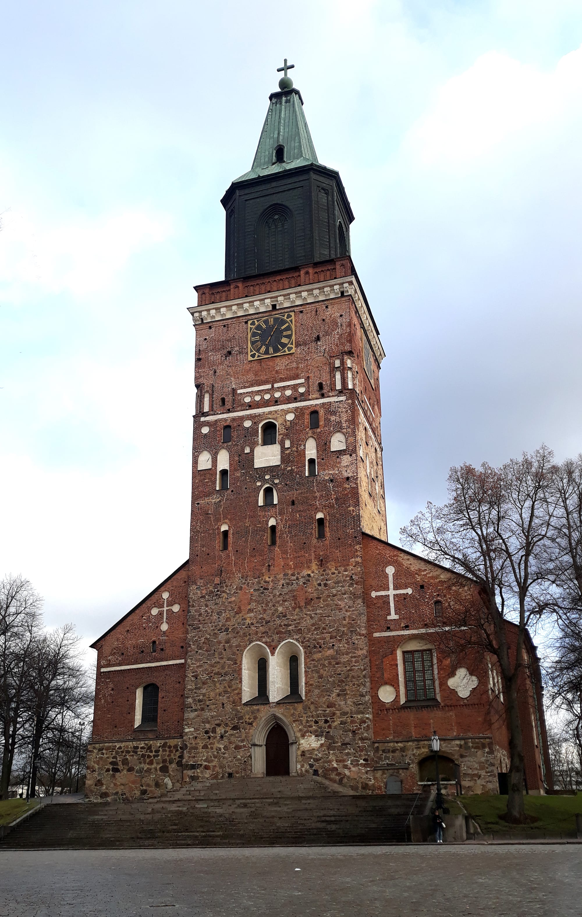 A tall red-brick medieval cathedral with a single square tower, seen across a river