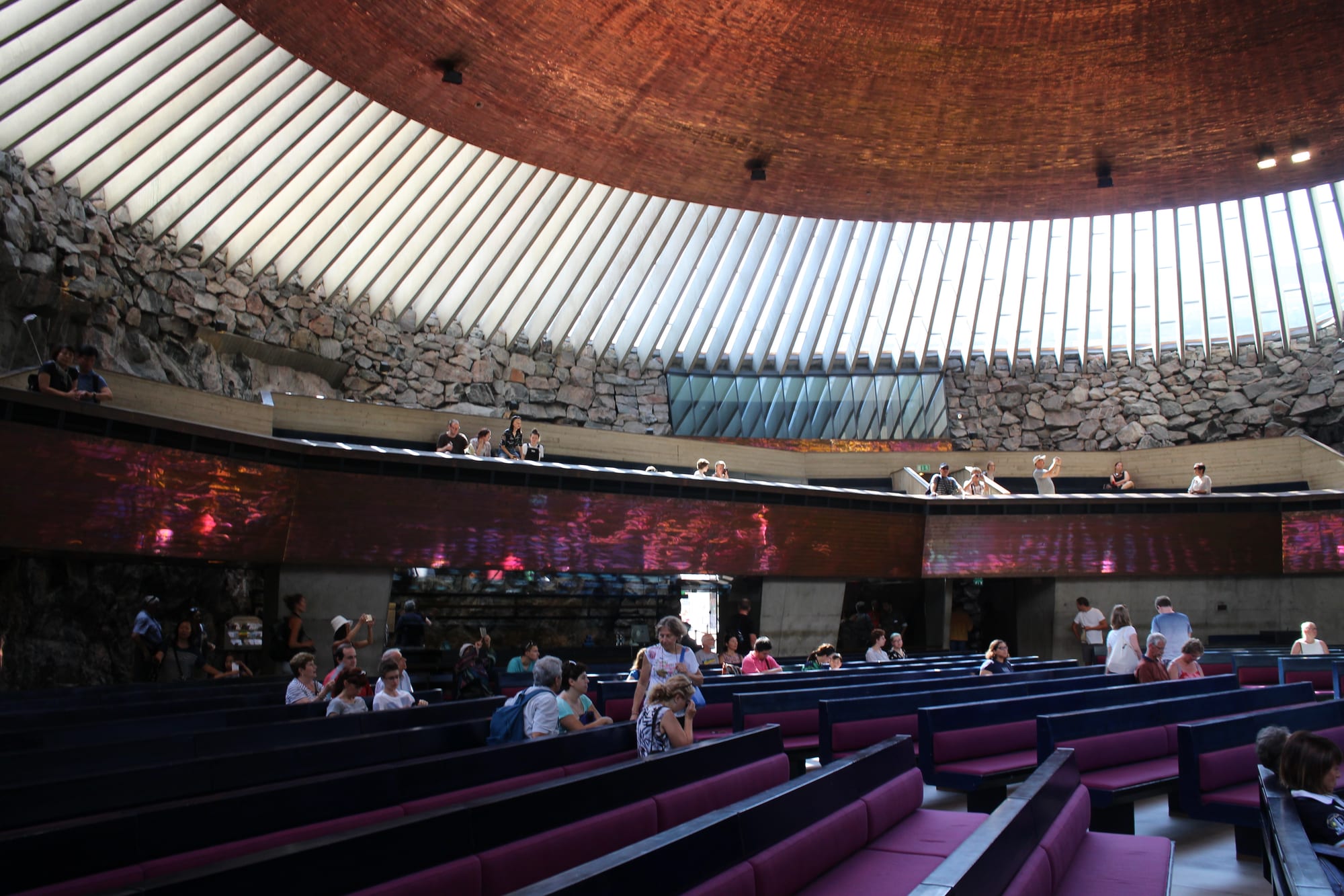 A circular church interior with rough rock walls and a domed copper ceiling on radial beams