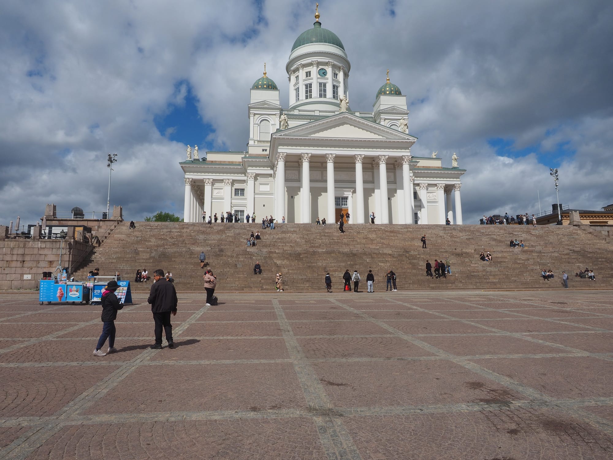 A white neoclassical cathedral with a green dome above a wide cobbled square