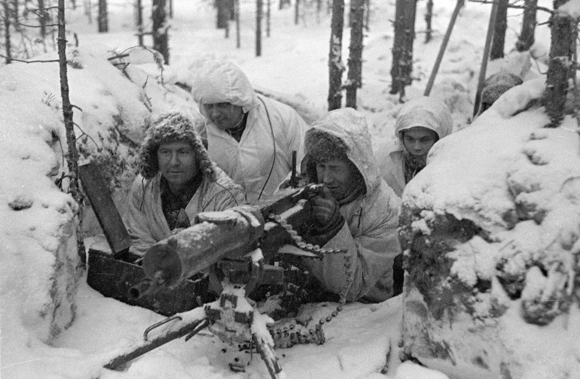 Finnish soldiers in white winter camouflage crouched behind a machine gun in deep snow