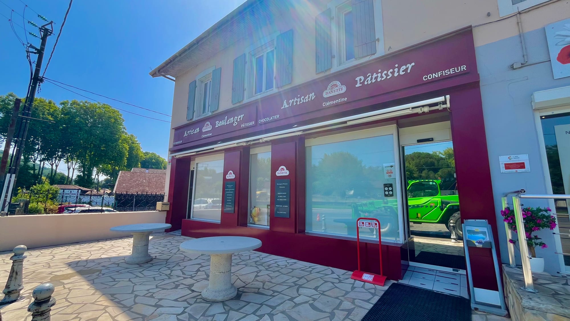 A French village bakery shopfront with striped awning and outdoor tables, reading Artisan Boulanger Pâtissier