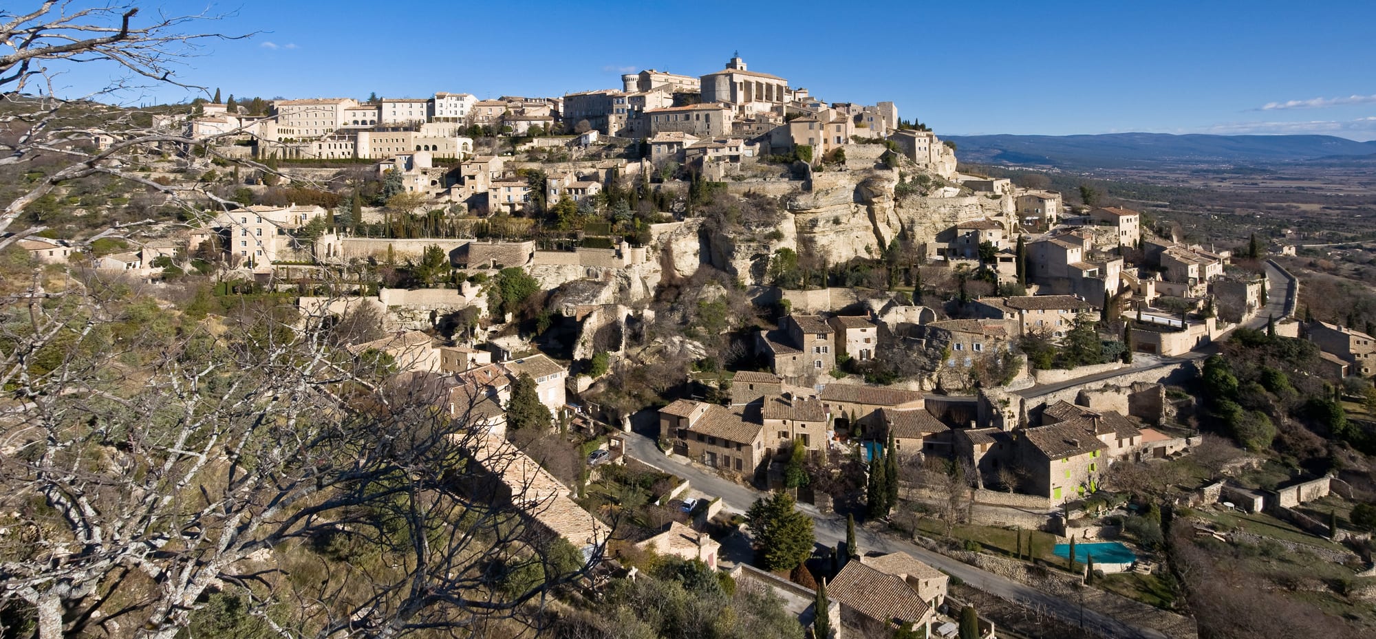 A stone hilltop village of pale houses stacked below a church and castle, fields below