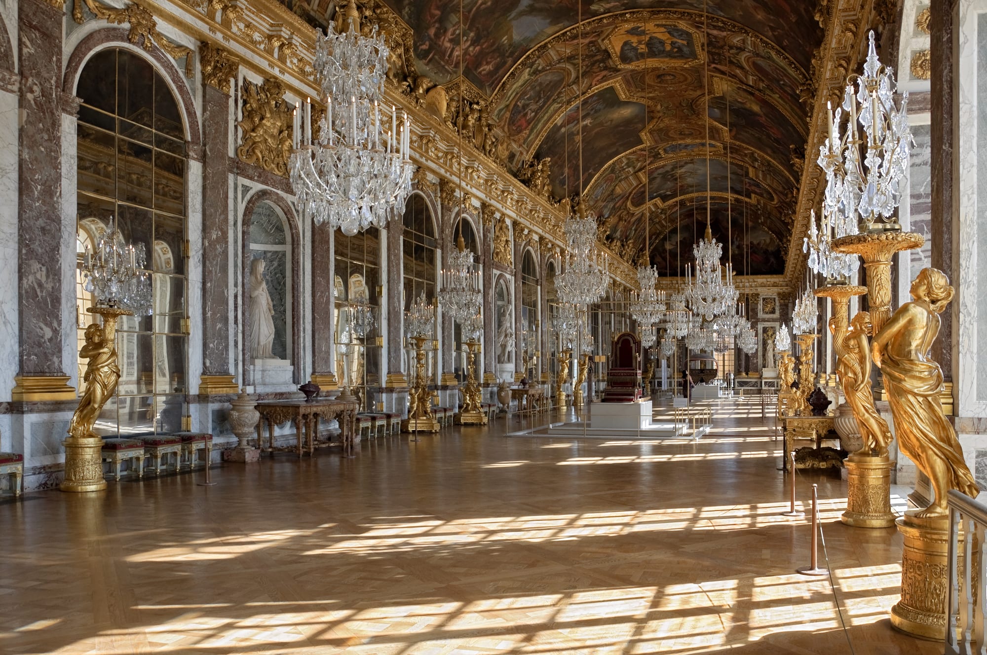 A long baroque gallery lined with arched mirrors and gilded statues under a painted ceiling