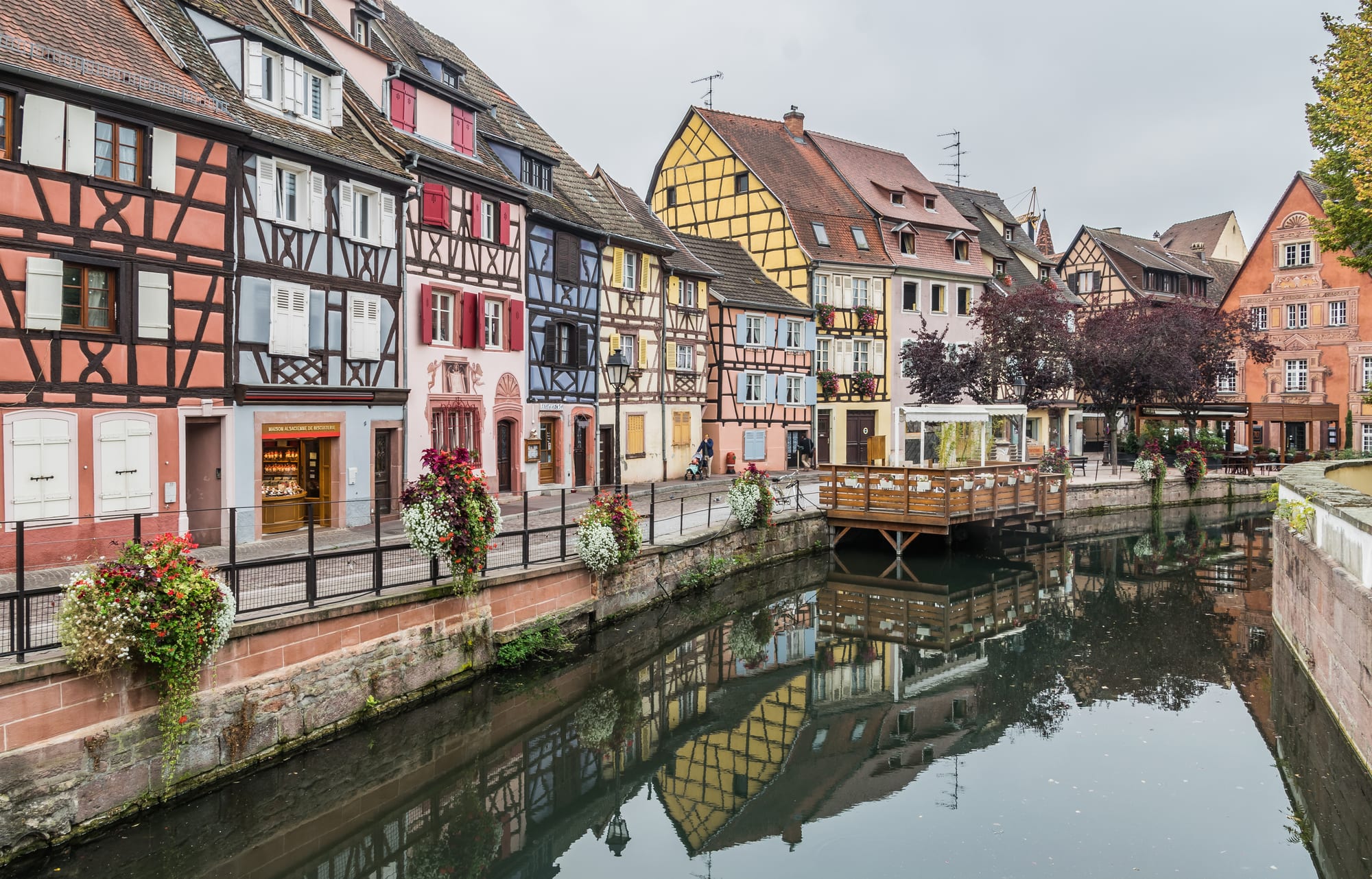 Timber-framed, brightly painted houses leaning over a narrow canal lined with flowers