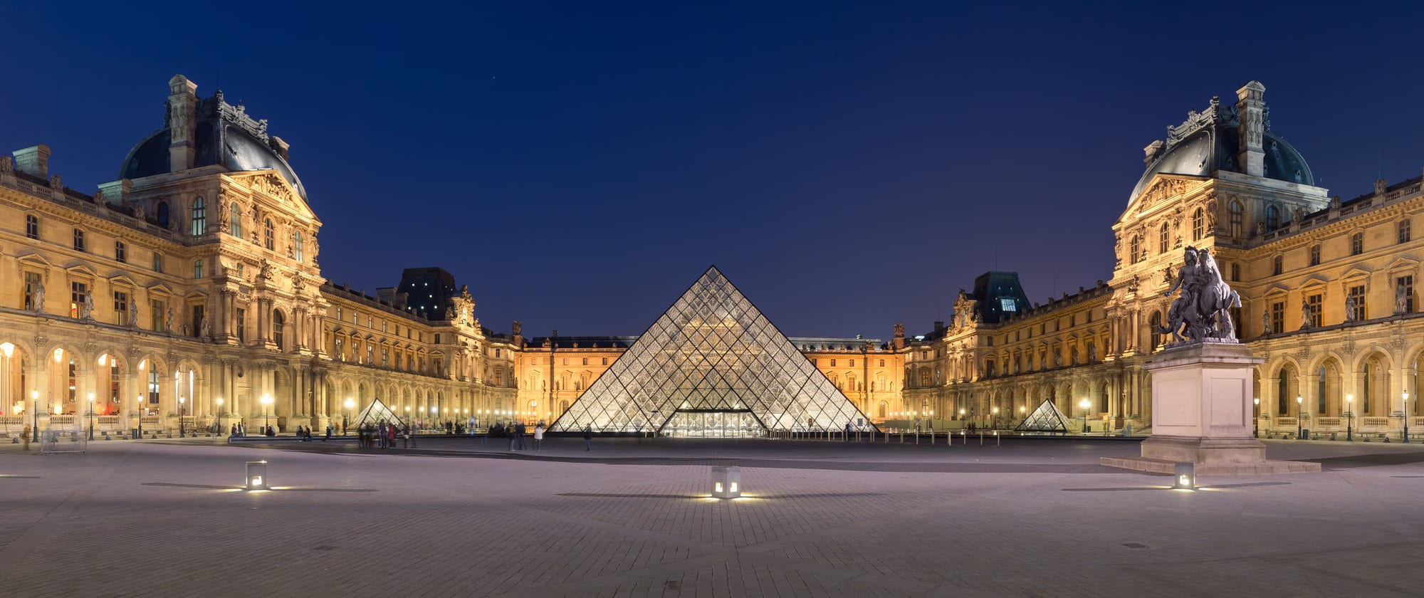 A grand palace courtyard with a large glass pyramid in the centre