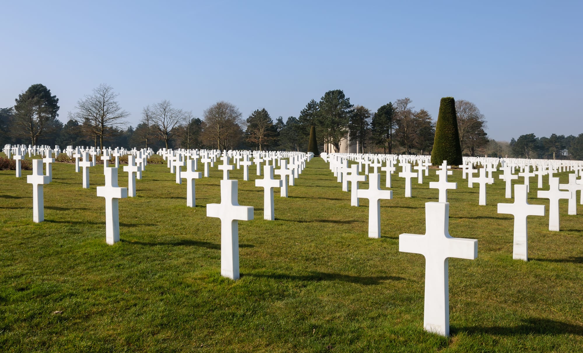 Rows of white marble crosses on a clipped green lawn above the sea