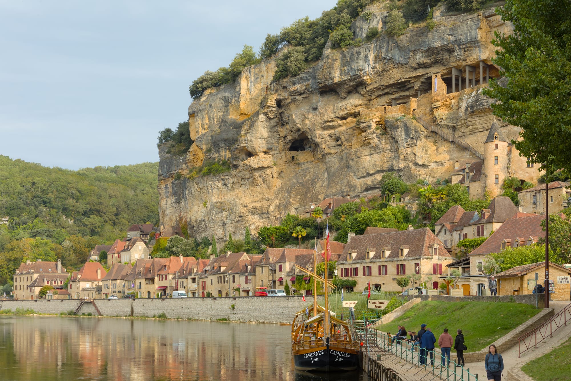 A village of golden stone houses pressed between a cliff and a calm river