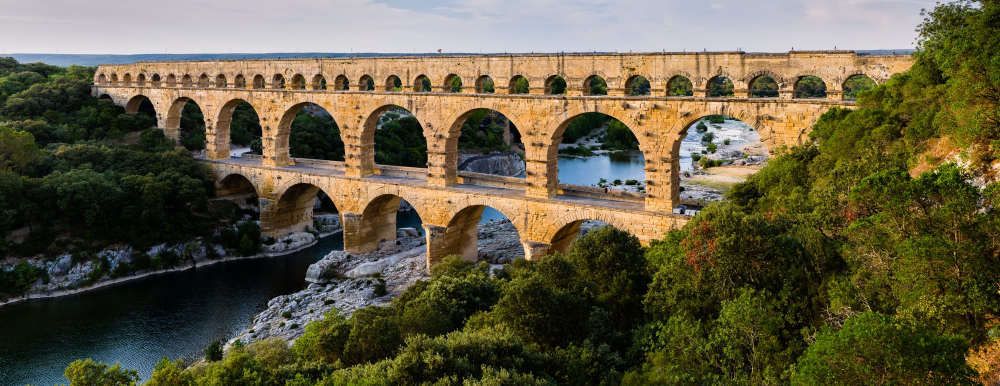 A three-tiered honey-coloured Roman arched bridge spanning a green river