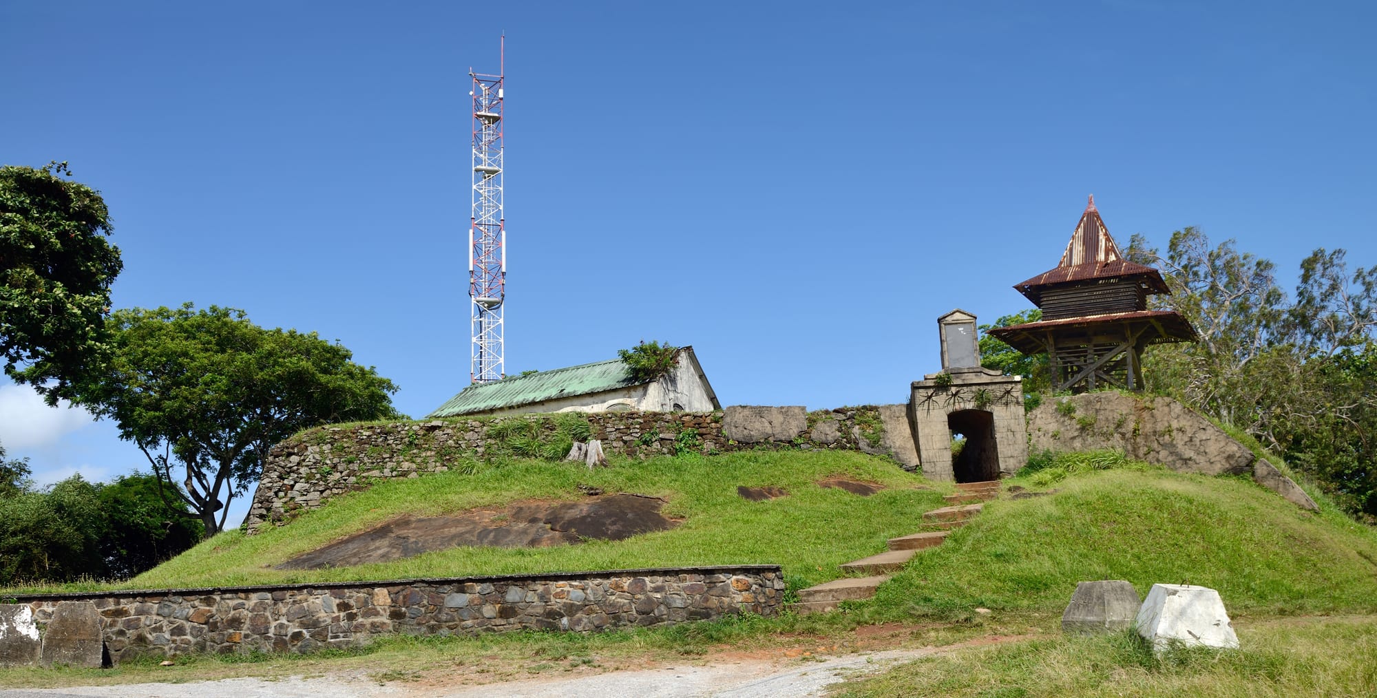 Low stone ramparts on a green hill overlooking a tropical town and estuary