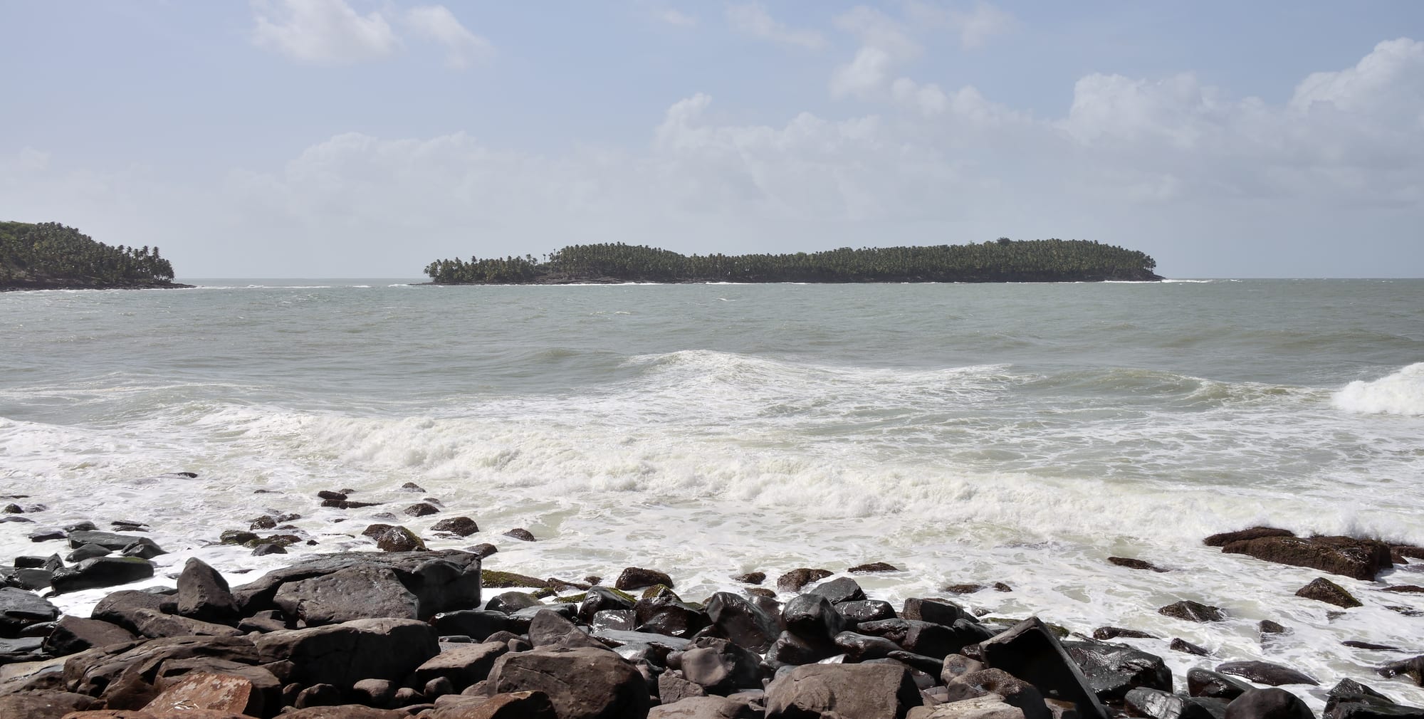 A small palm-covered island with a few colonial buildings, seen across choppy water