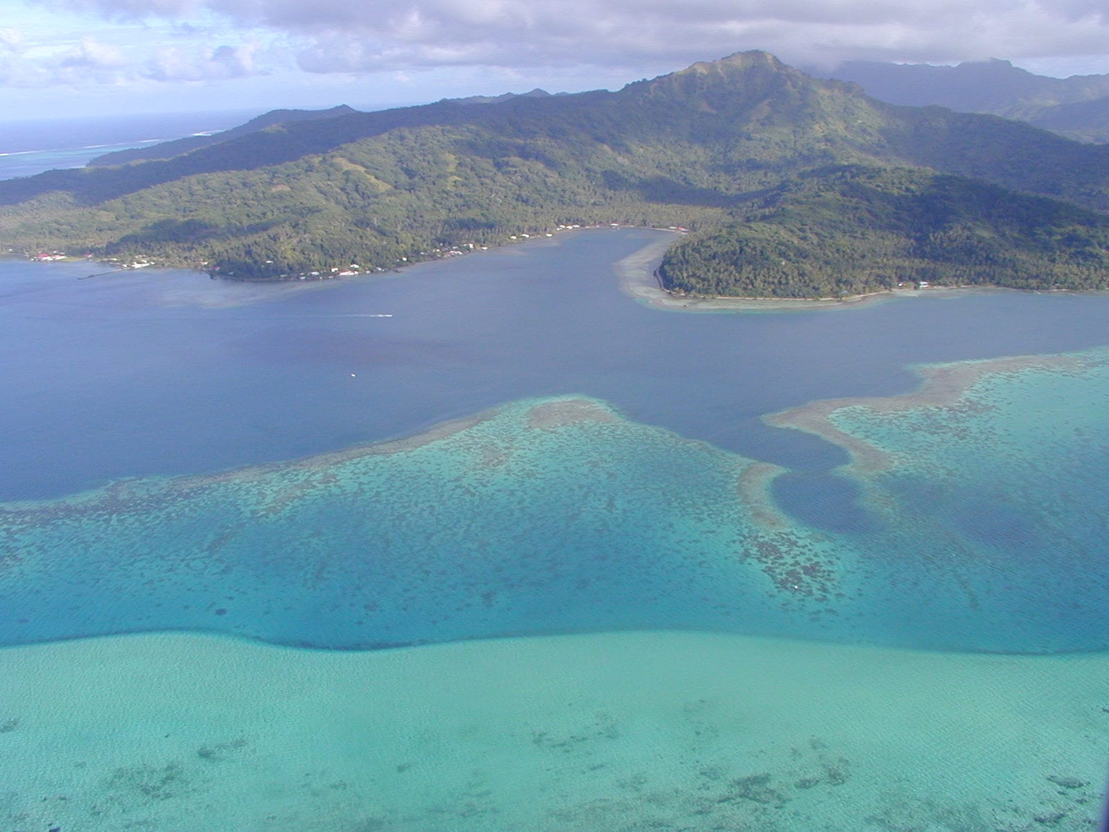 An aerial view of an island and its wide reef-enclosed lagoon dotted with motu