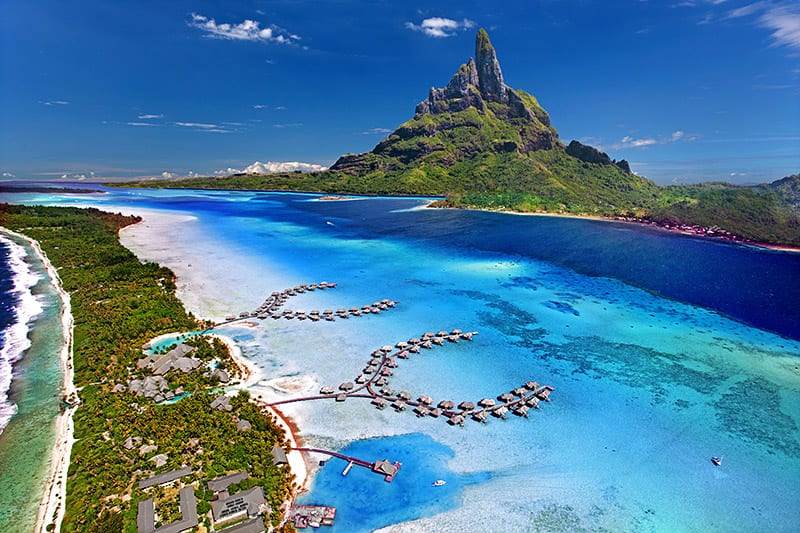 A jagged green peak on an island ringed by a bright turquoise lagoon and reef