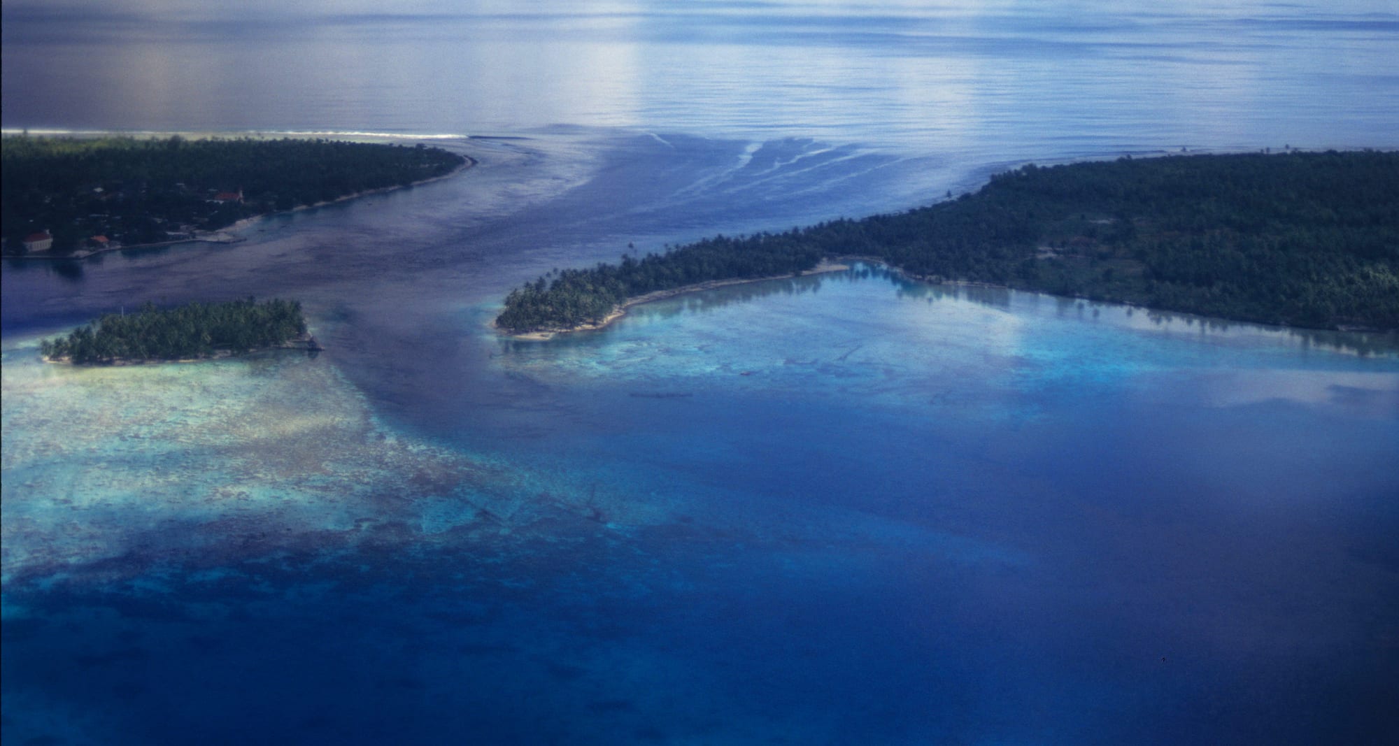 A shallow reef pass with fast blue water flowing between coral flats