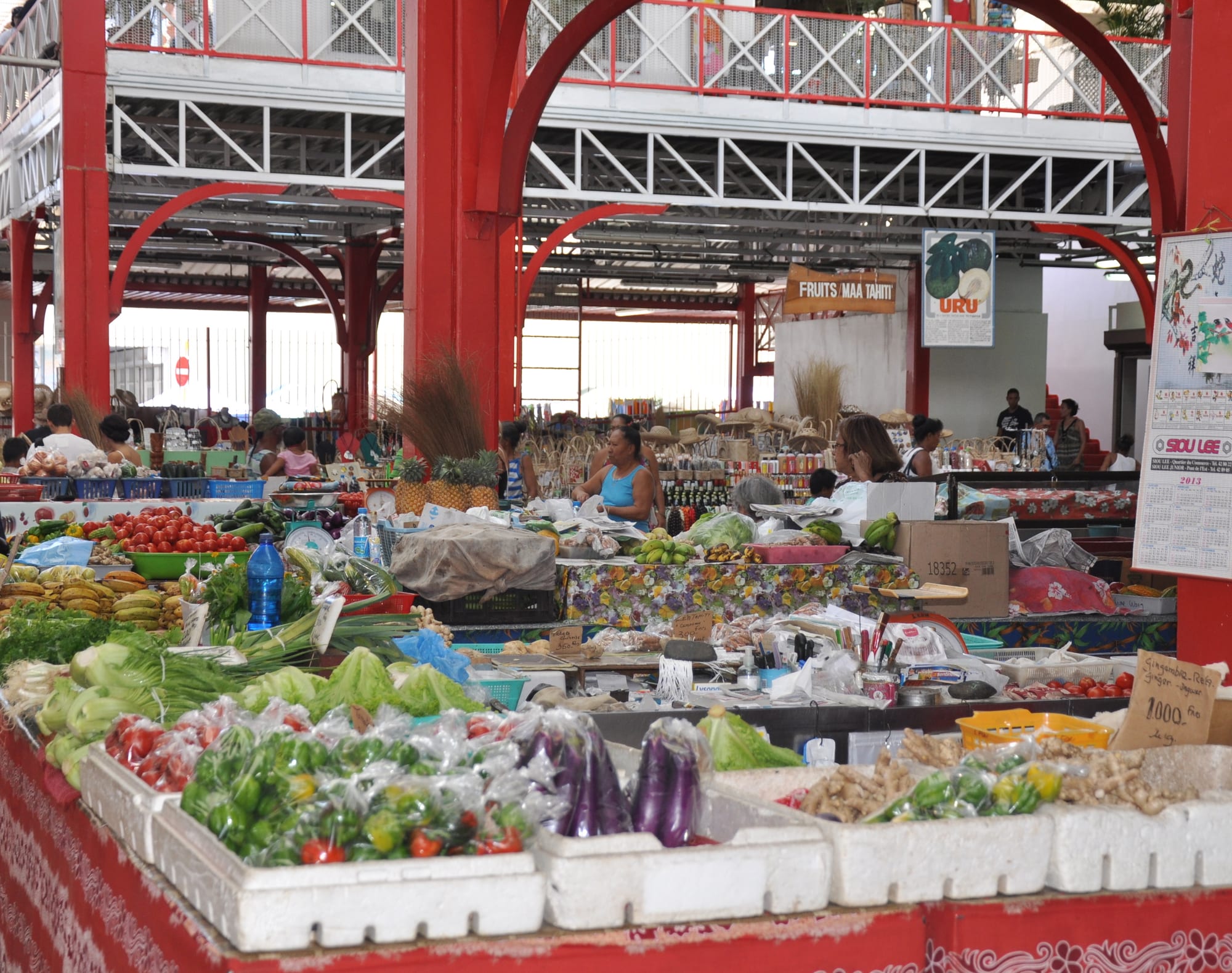 The covered municipal market in Papeete, Tahiti, with stalls piled high with tomatoes, greens, bananas and other produce, and shoppers browsing