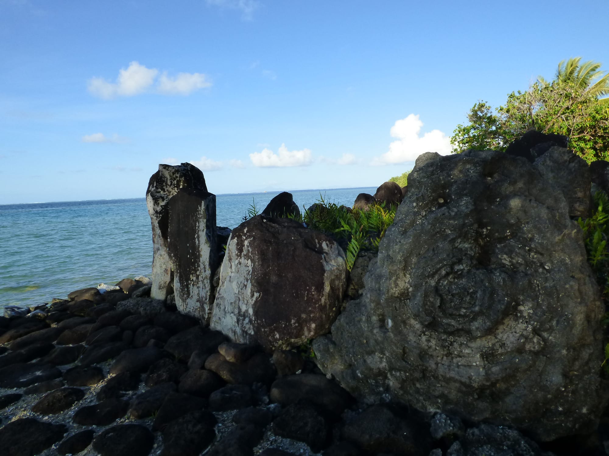 A large low platform of stacked dark stones with tall upright slabs, beside a lagoon