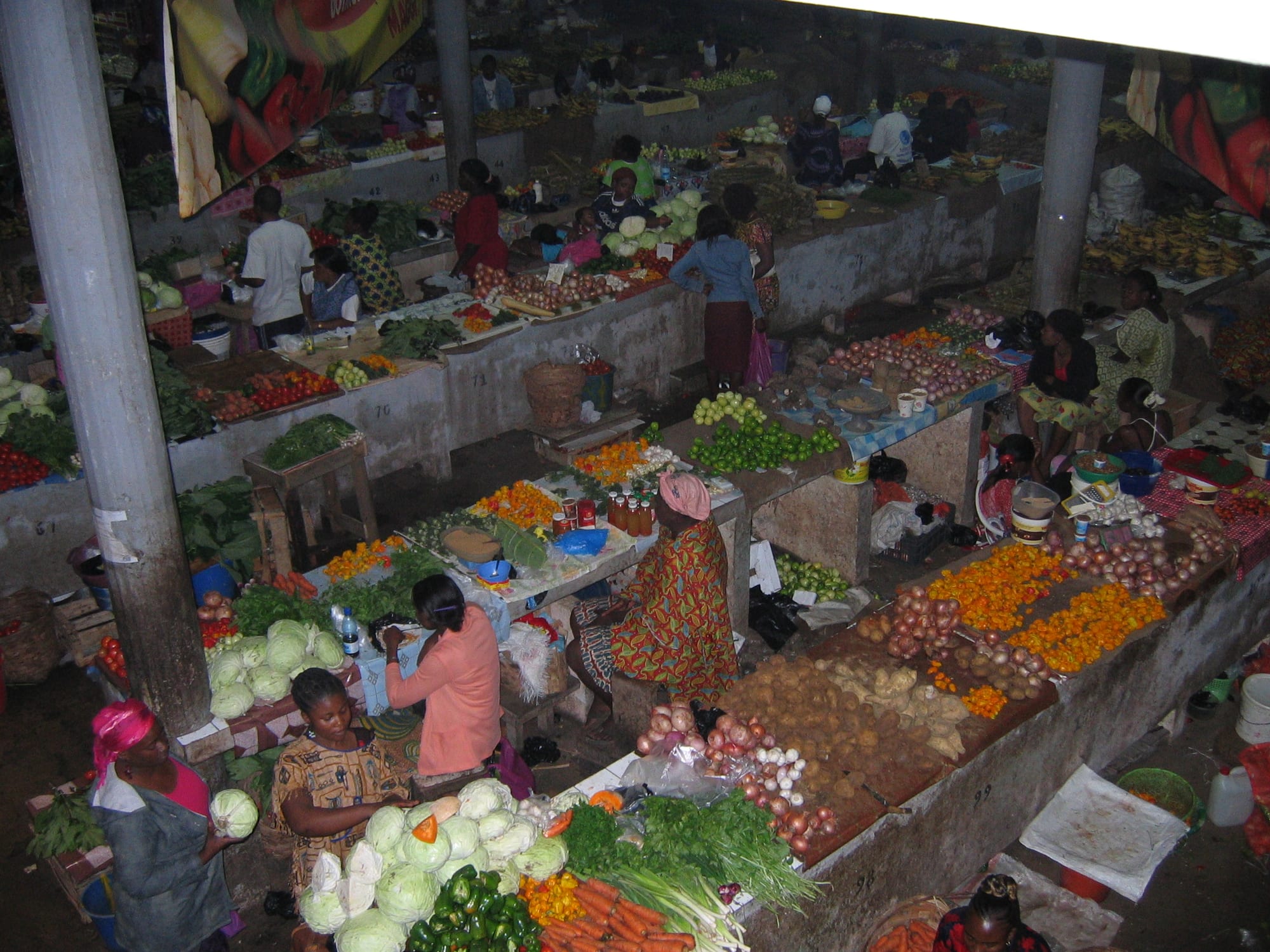 Vendors and shoppers among stalls of vegetables, onions and fruit under a covered market roof in Libreville