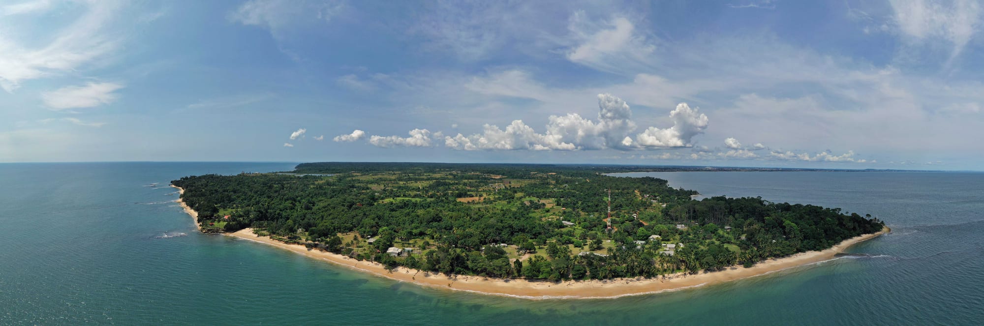 A calm bay with a rocky point, low buildings, and forest along the shore