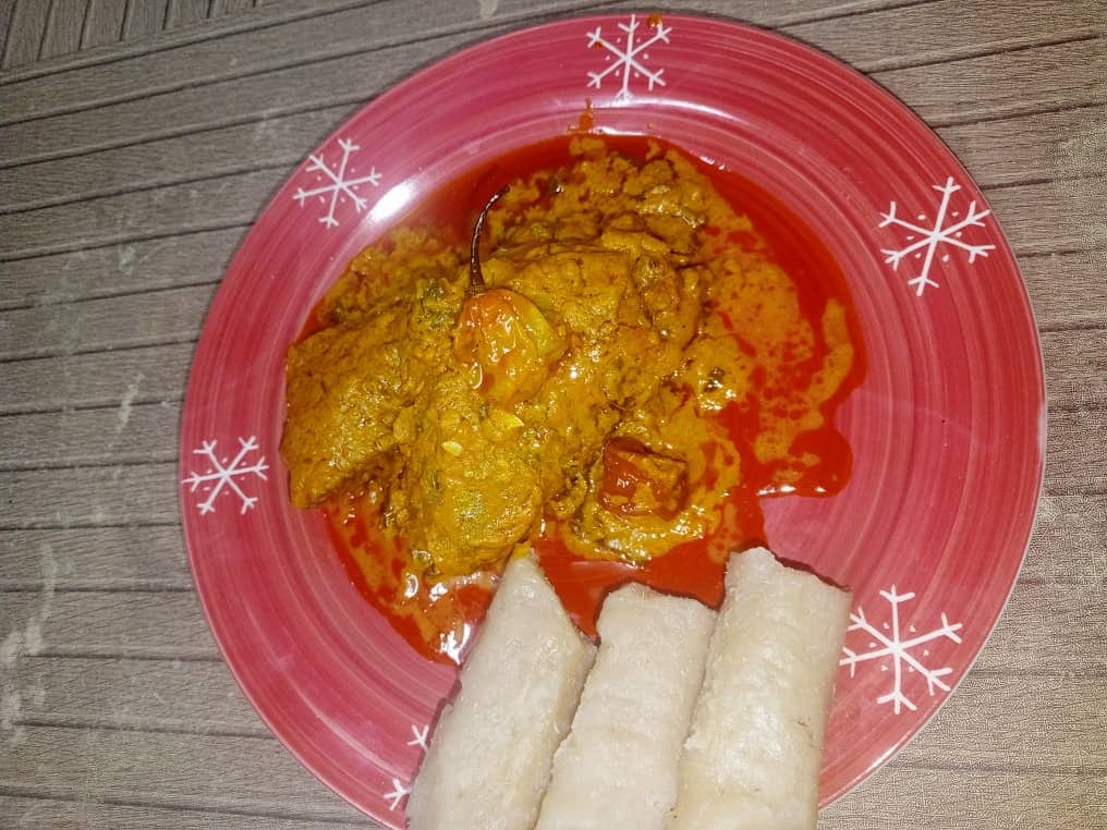 A stew of chicken in a thick orange-red sauce, served with a starch