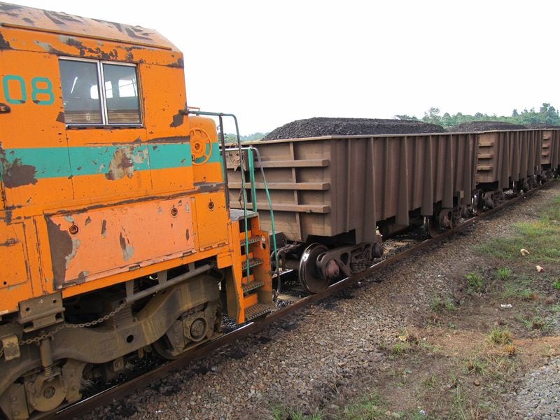 A long train loaded with manganese ore on a single-track railway through green forest