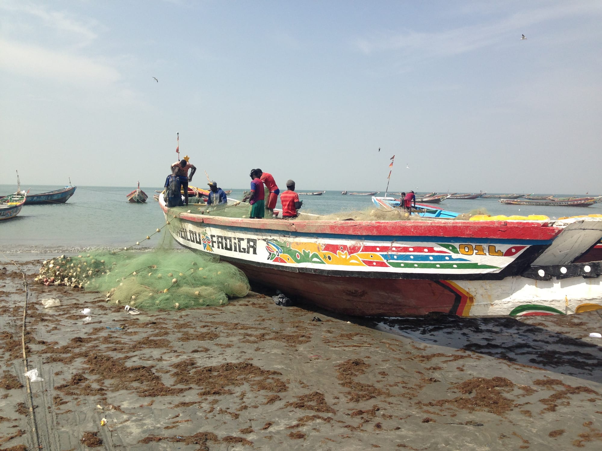 A brightly painted wooden fishing boat on a busy beach with people unloading