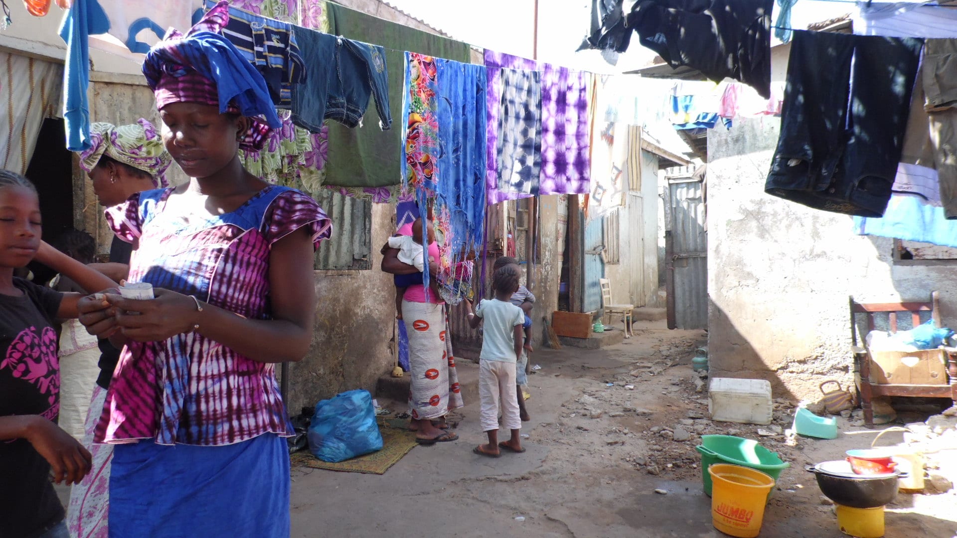 Women and children in a narrow compound yard hung with drying laundry between simple block houses