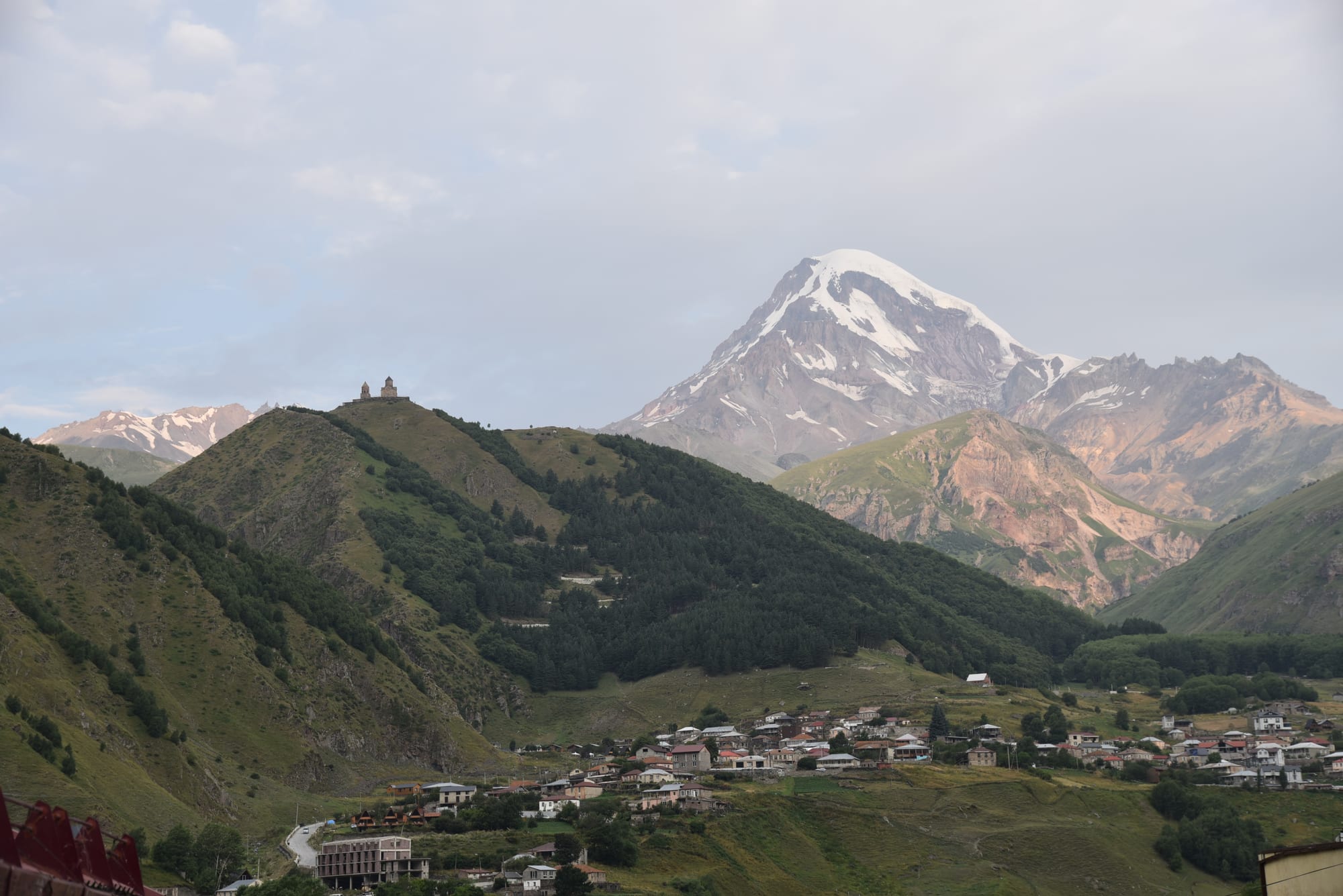 A lone medieval church on a green ridge with a huge glaciated peak behind