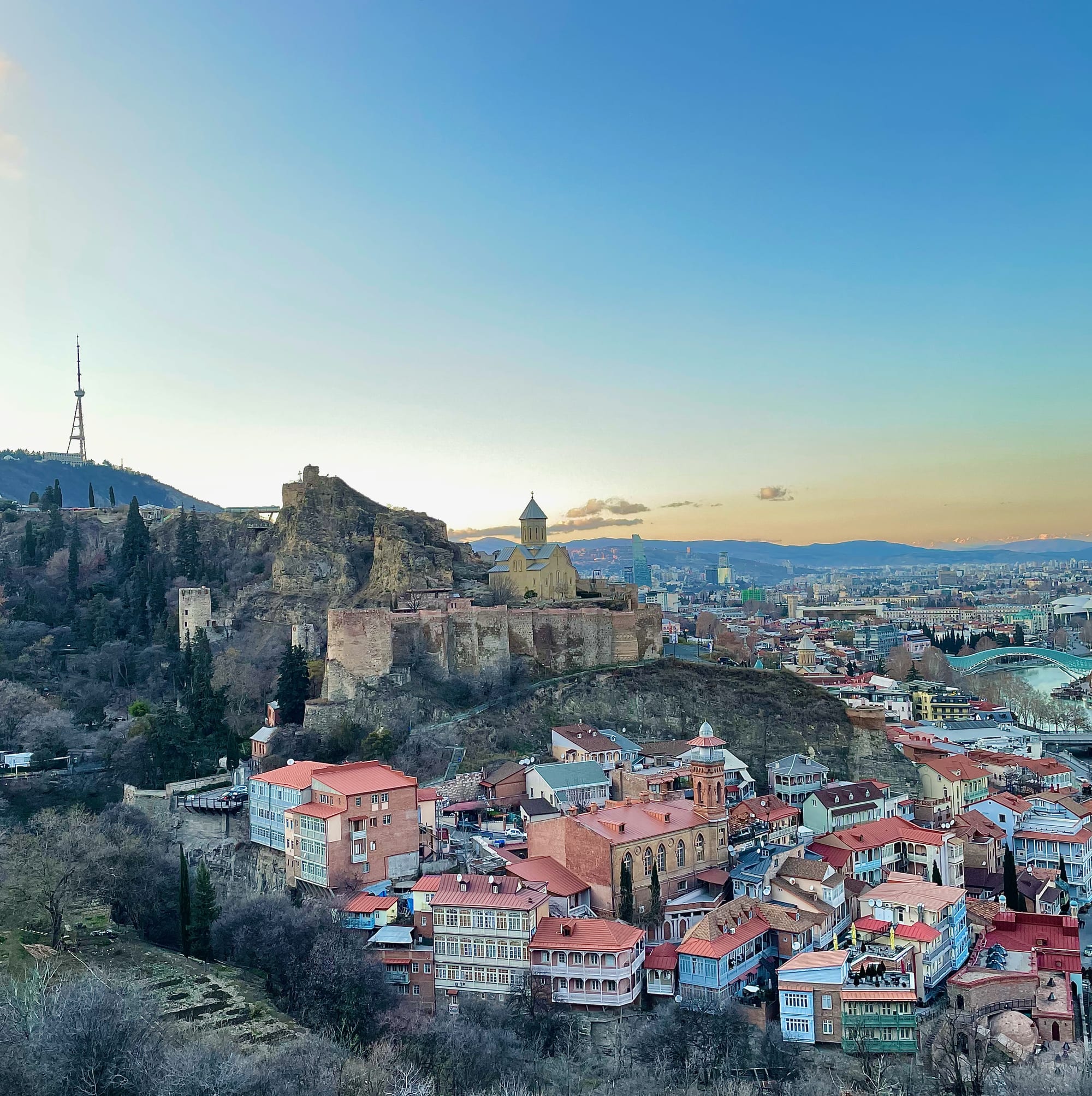 A hillside old town of tiled roofs and carved wooden balconies below a fortress