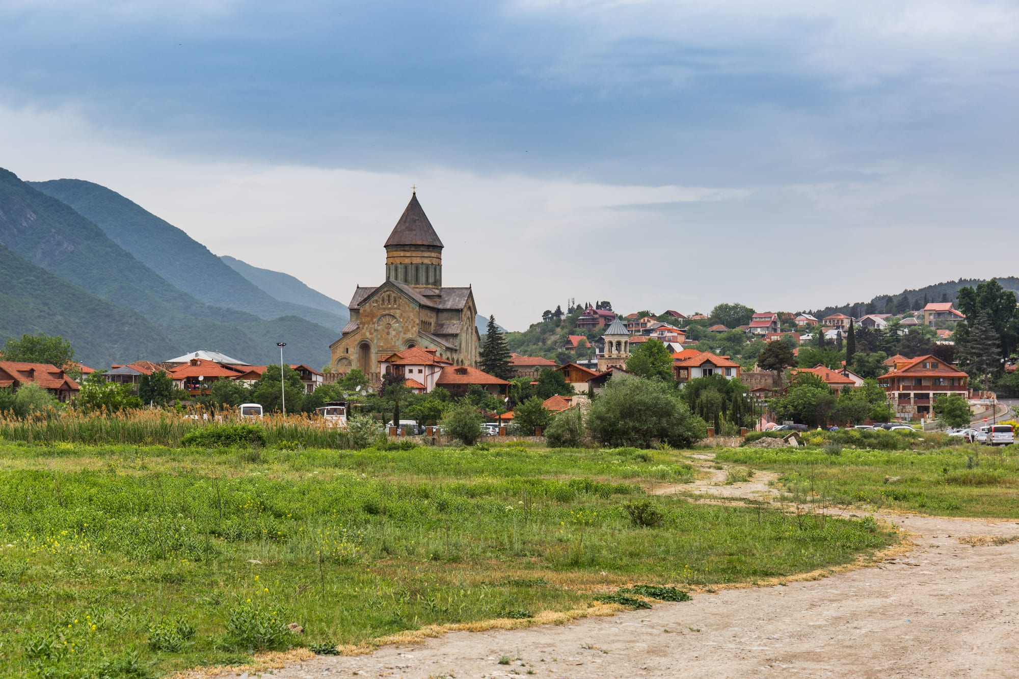 A large medieval stone cathedral with a conical dome inside crenellated walls, mountains behind