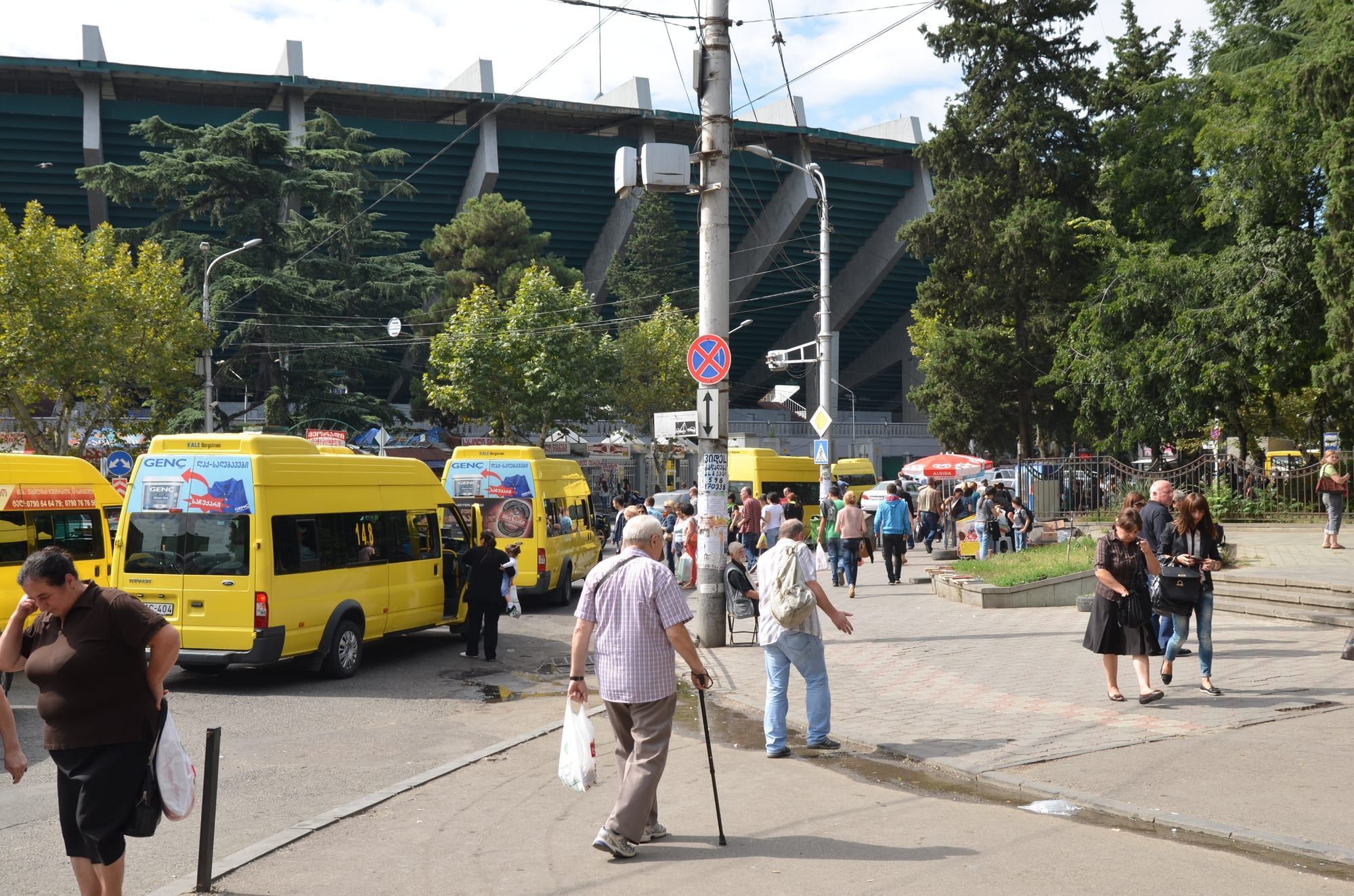 Rows of yellow marshrutka minibuses parked at a Tbilisi terminus with pedestrians crossing the street nearby
