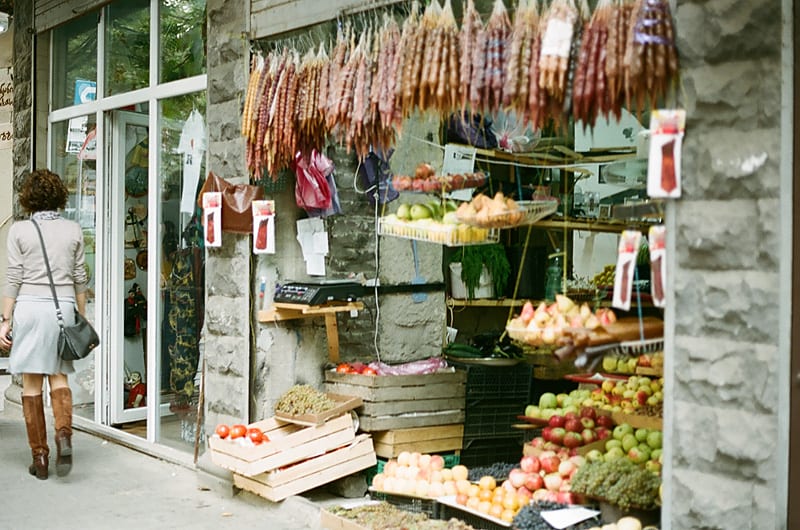 A small street-front fruit shop in Tbilisi with dried churchkhela sweets hanging above crates of fresh fruit