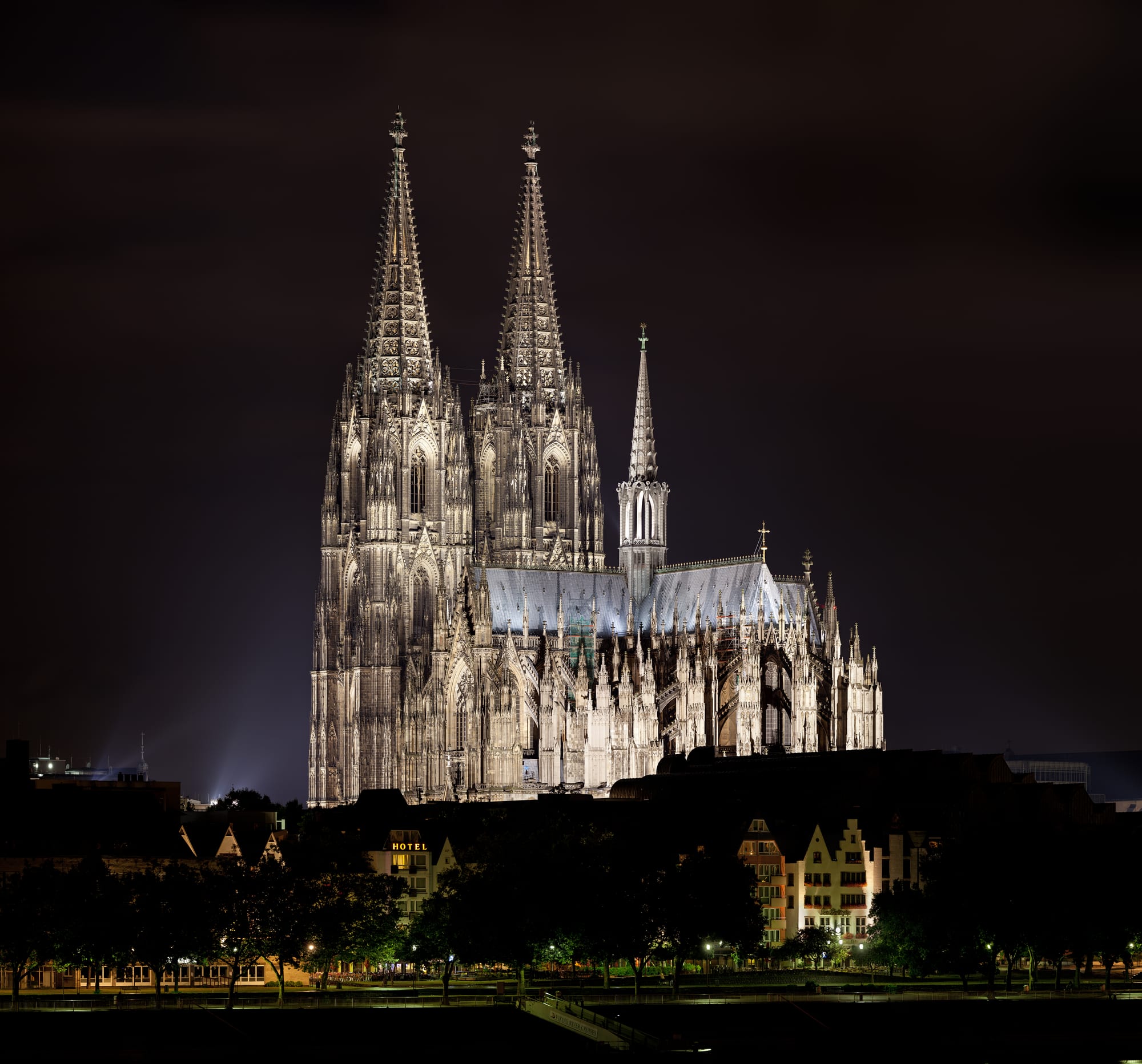 A vast twin-spired Gothic cathedral floodlit at night above a city square