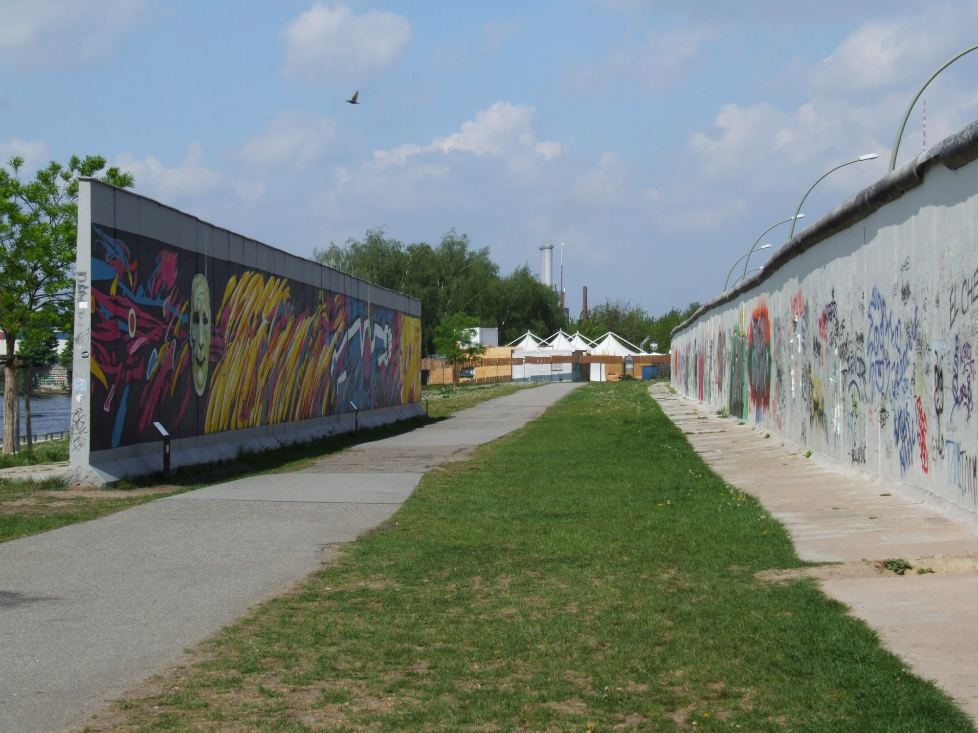 A long concrete wall covered in murals beside a river and a road