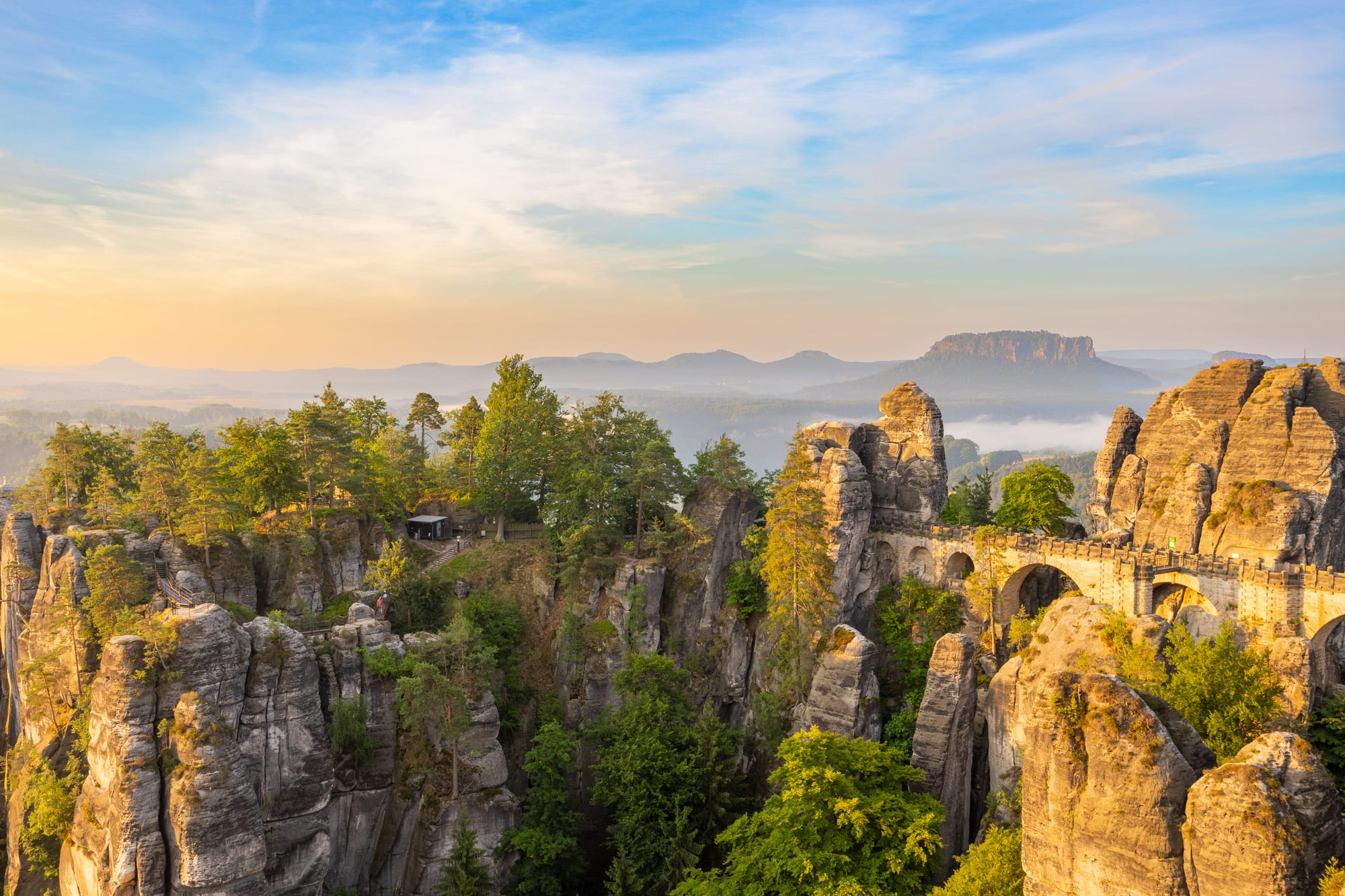 A stone footbridge linking tall sandstone pinnacles above a forested valley