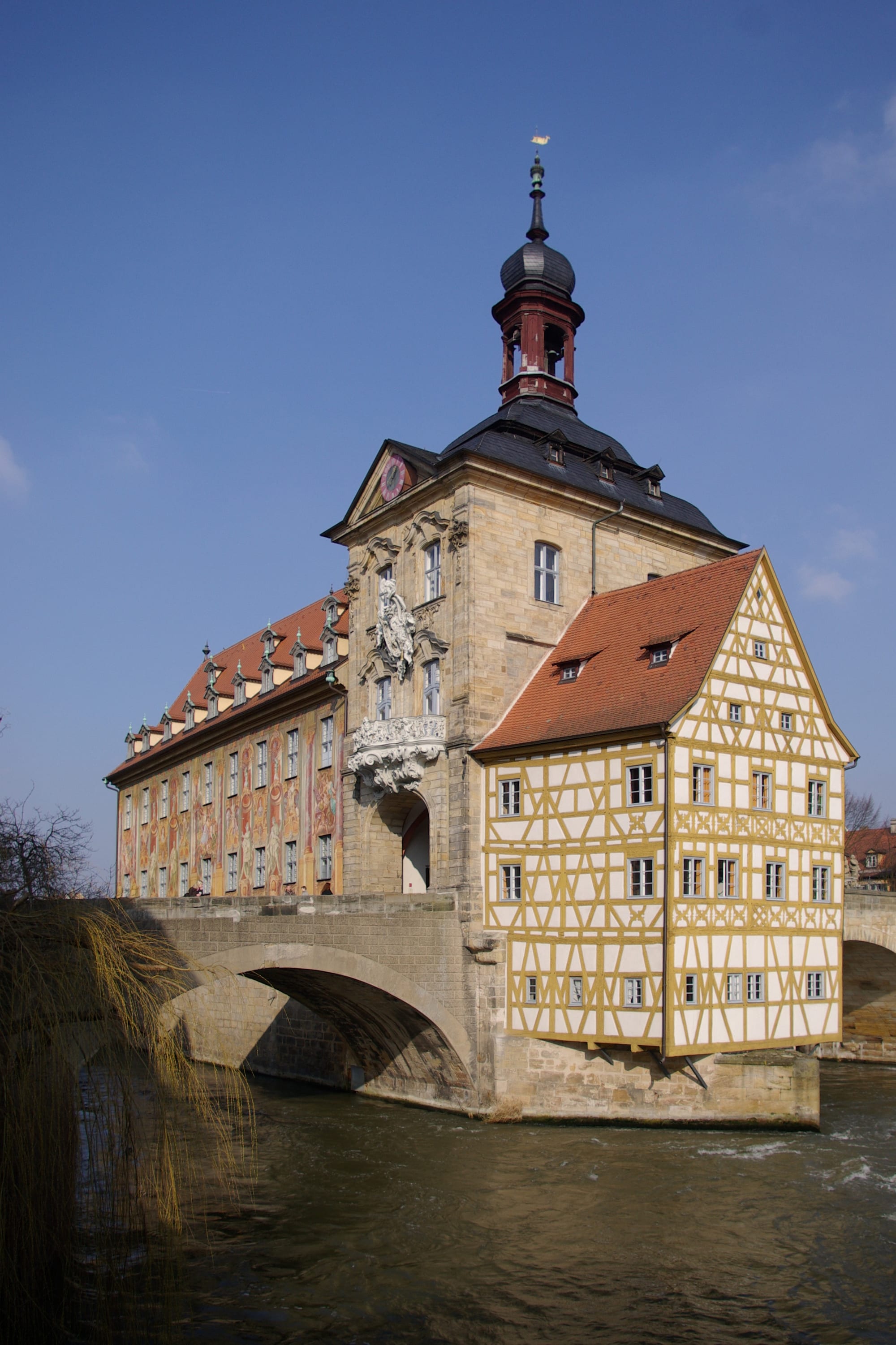 A painted half-timbered town hall built on a bridge over a river