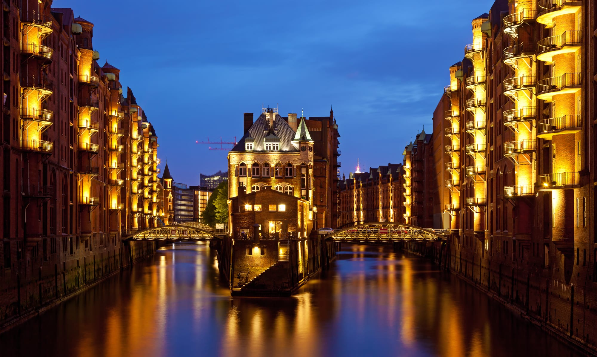 Red-brick warehouse blocks with gables and turrets along floodlit canals at dusk