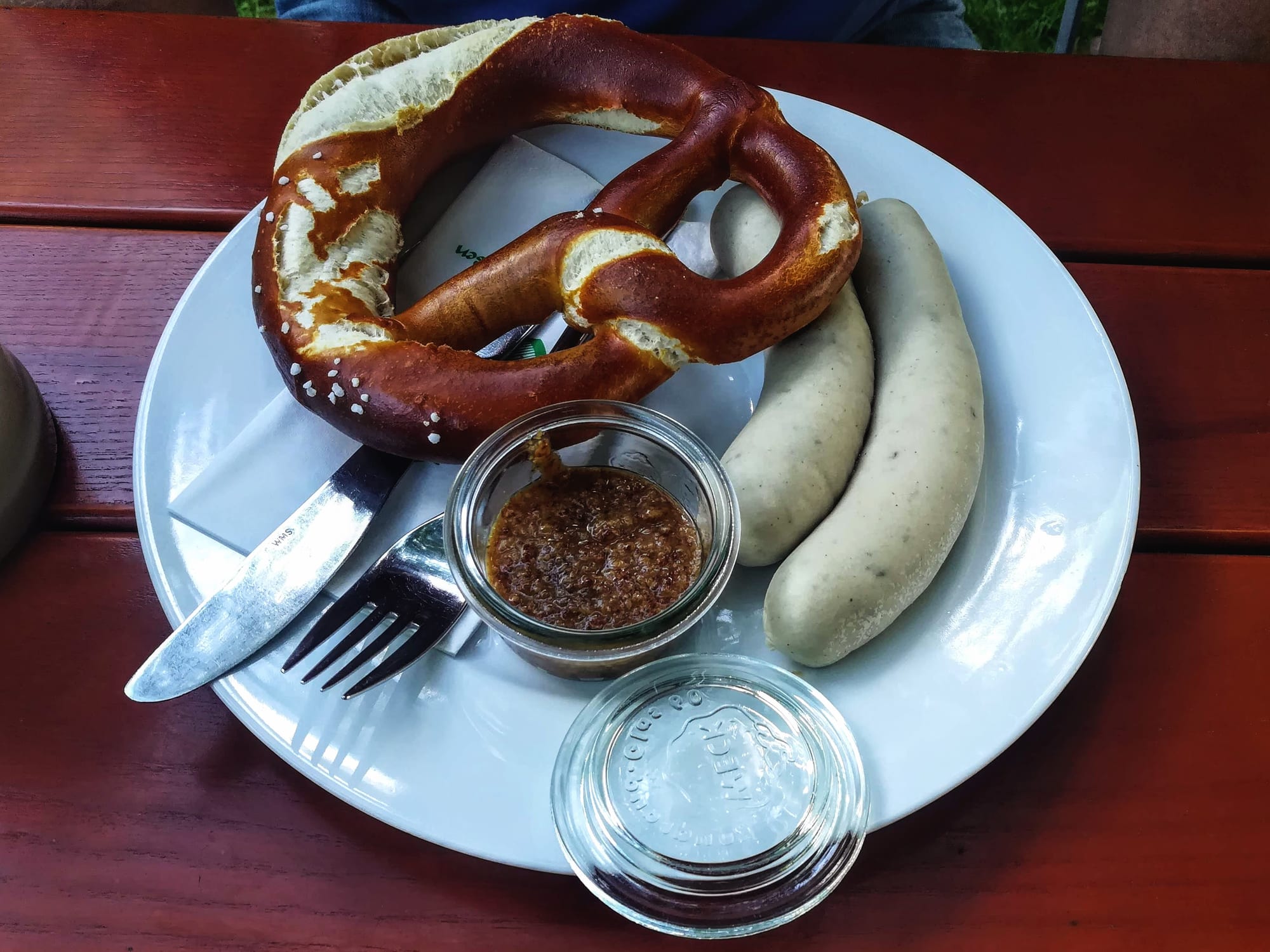 A plate of white sausages, a pretzel and mustard on an outdoor table
