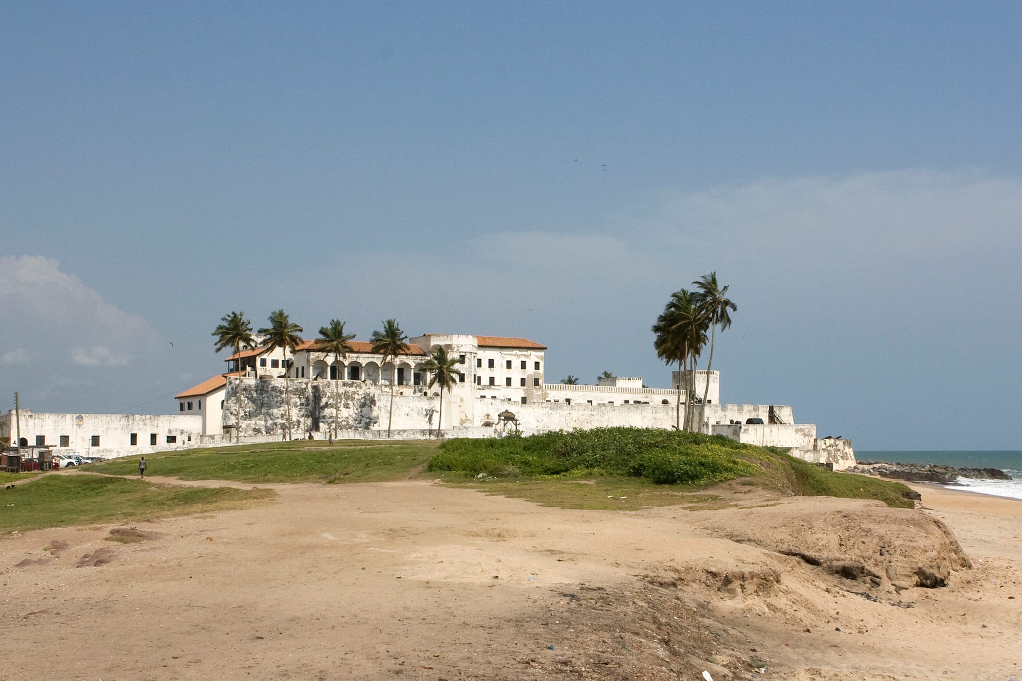 A massive white fort on a spit of land, with fishing boats crowding the water beside it