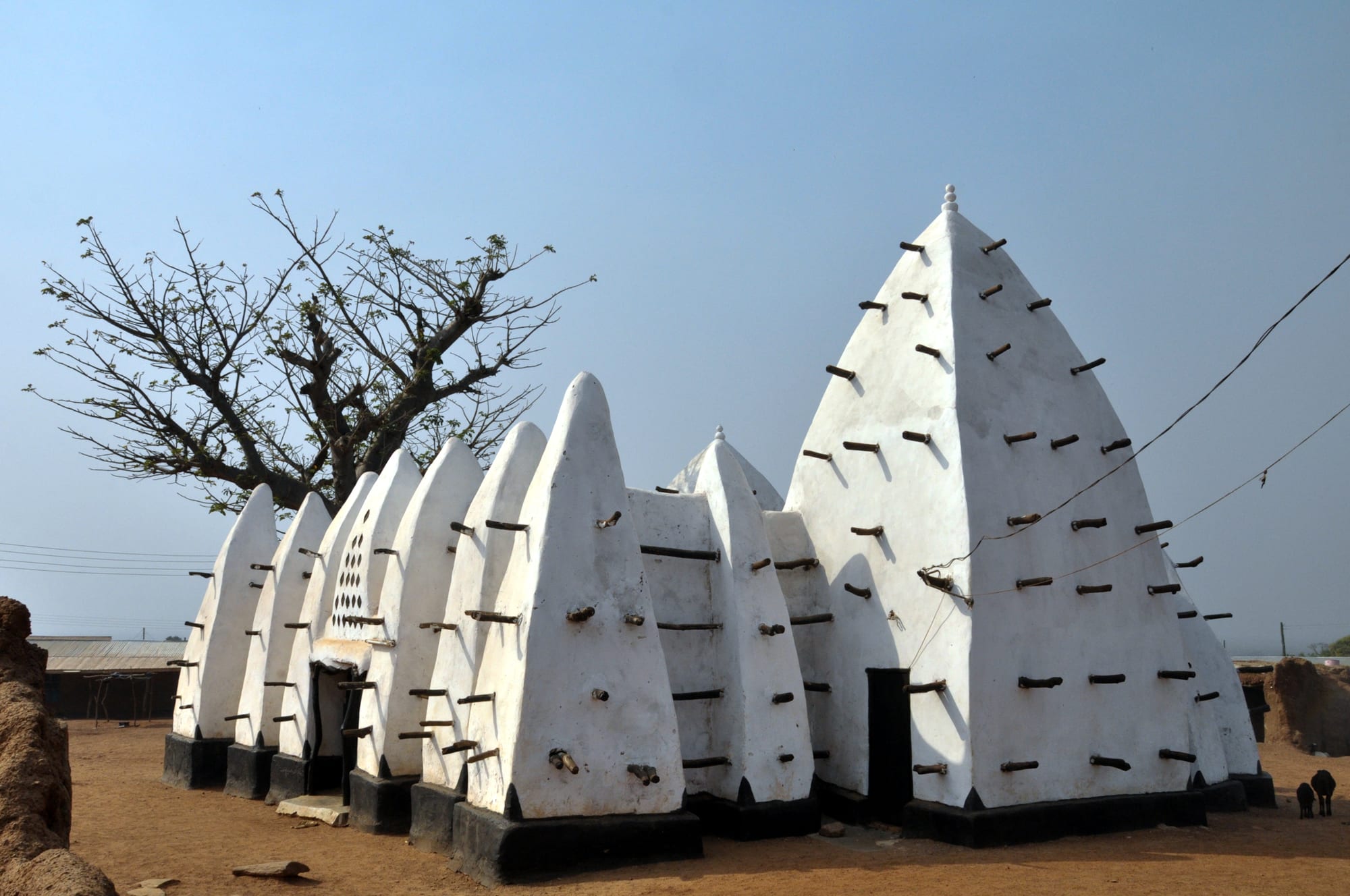 A small white mud mosque with buttressed walls and two pyramidal towers