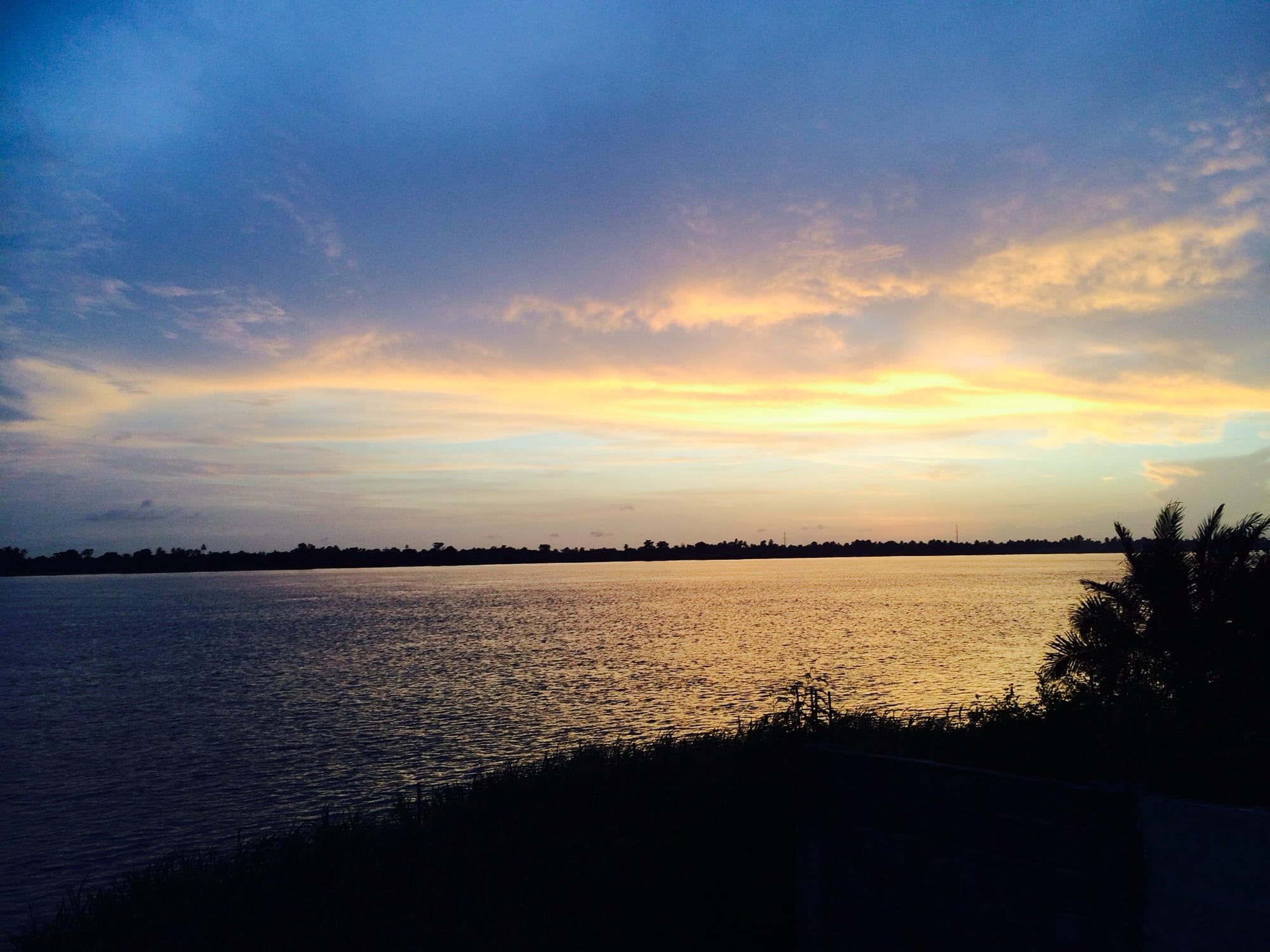 A wide lake glowing orange and gold at sunset, with a silhouetted tree line