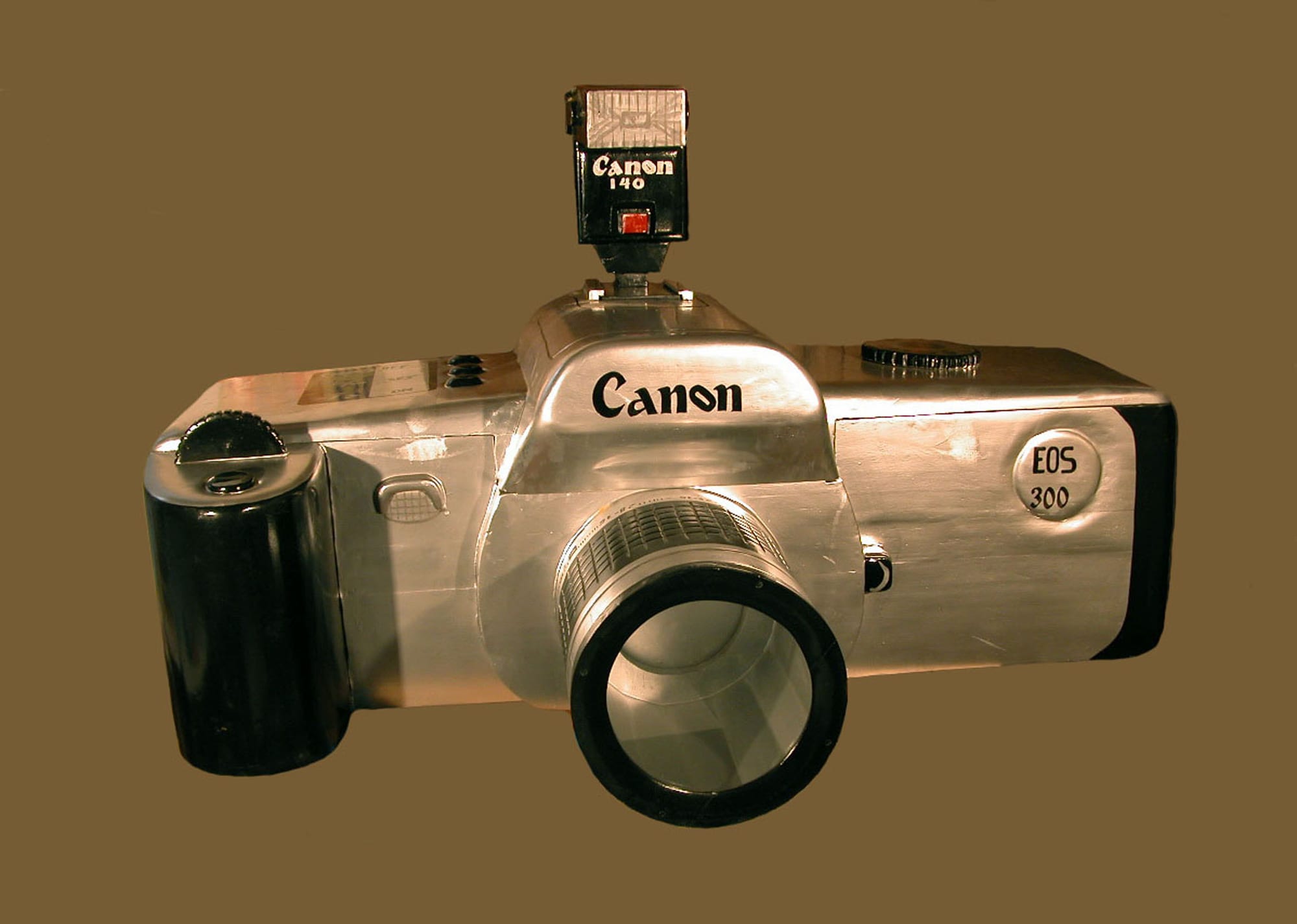A large wooden coffin carved and painted in silver and black to look exactly like a single-lens reflex camera, complete with lens and flash