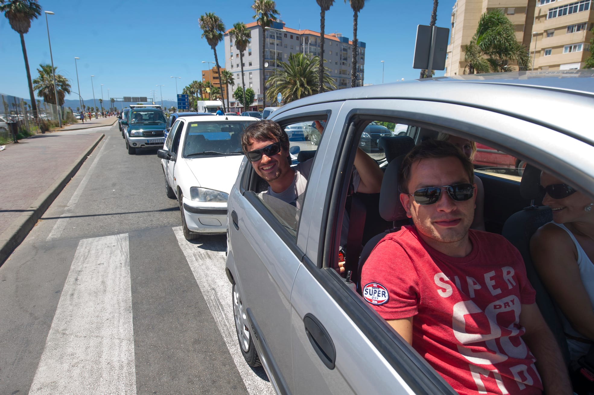 Cars queued at the Gibraltar-Spain border crossing with occupants looking out, apartment blocks and palm trees on the Spanish side behind