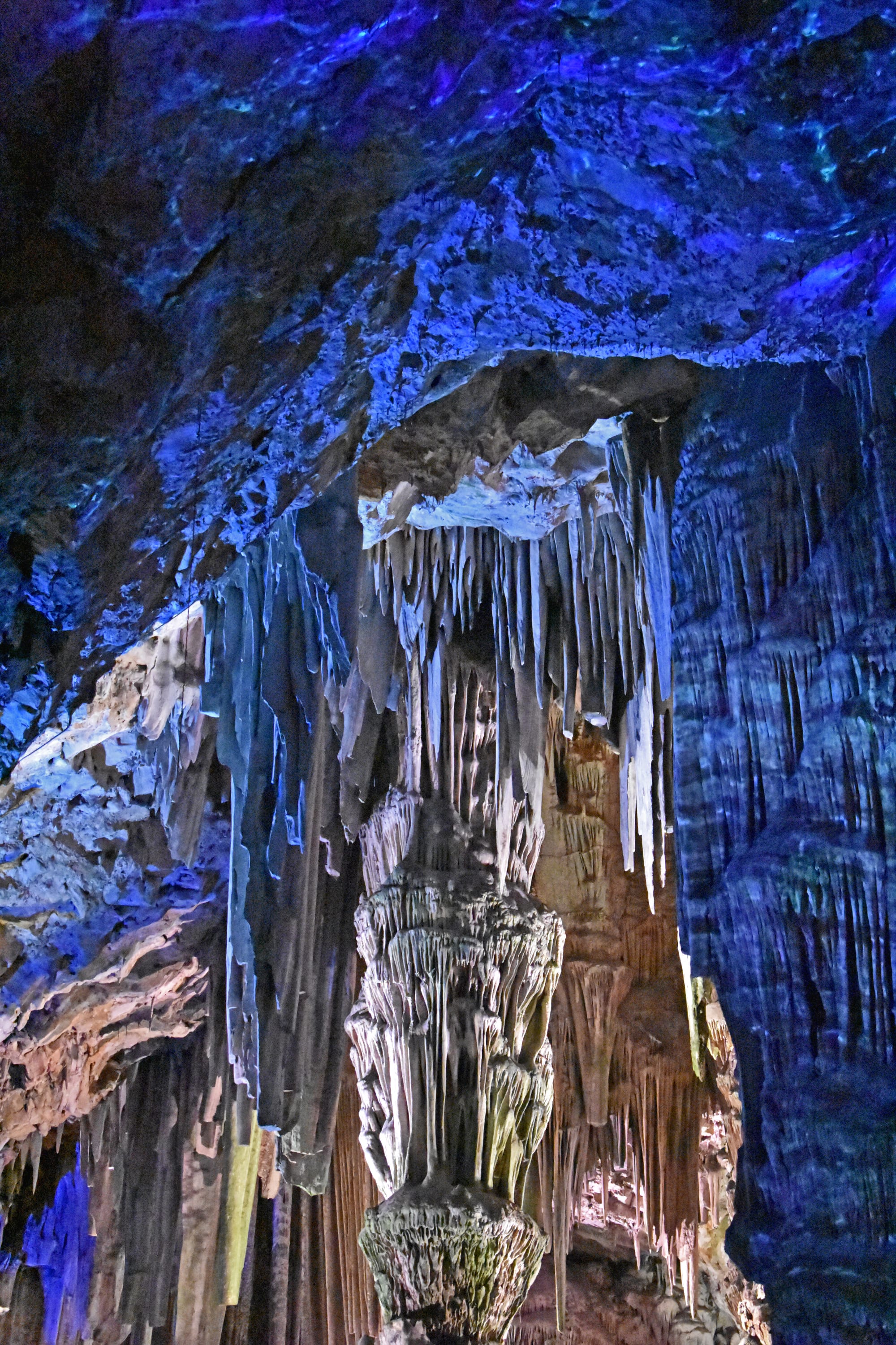 A large cave chamber of illuminated stalactites and flowstone, lit in colours