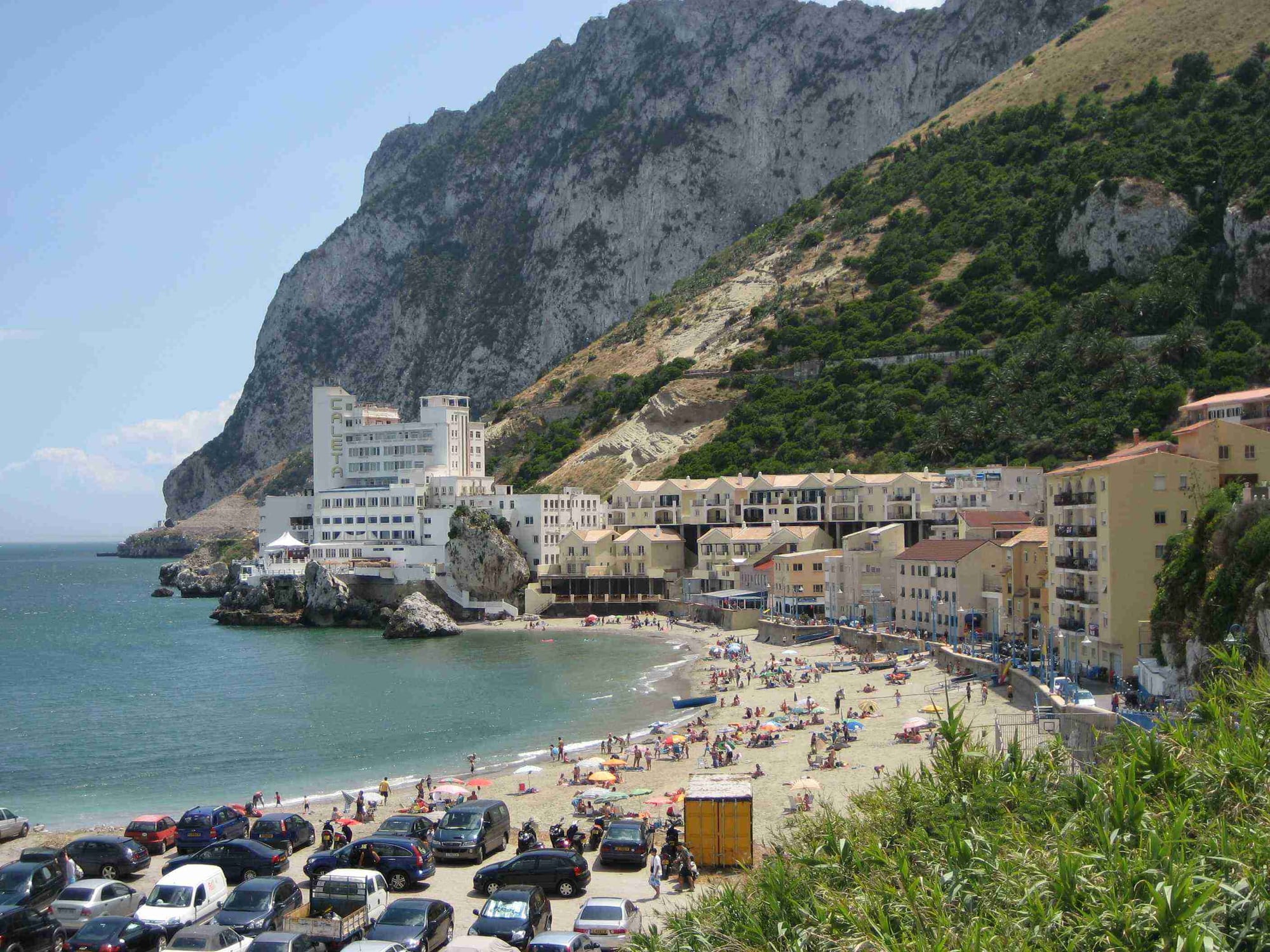 A small sandy cove with a cluster of houses beneath the steep eastern cliff of the Rock