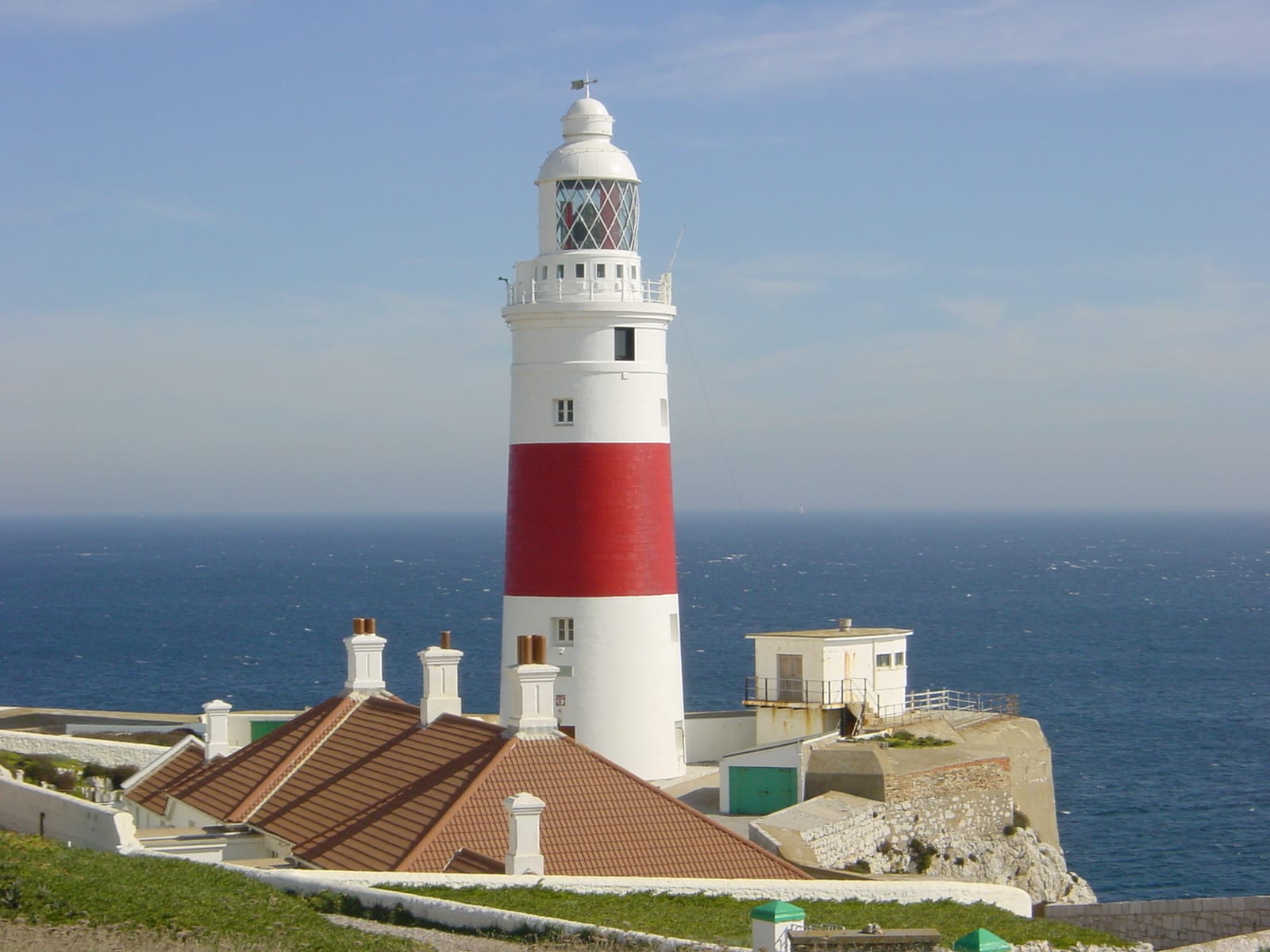 A red-and-white striped lighthouse on a low headland above the sea