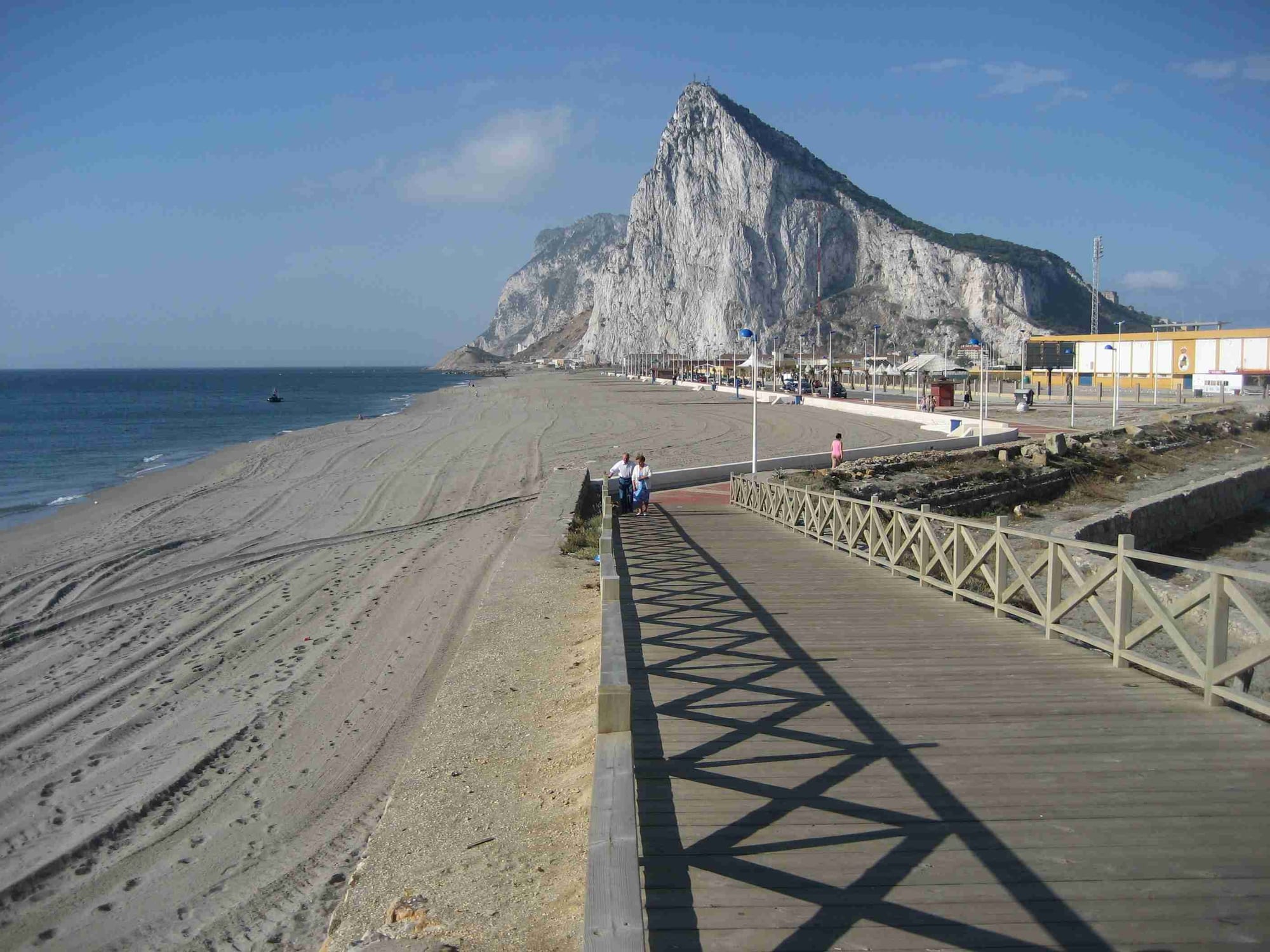 A steep grey limestone headland rising sharply from a flat sandy isthmus, town buildings at its base